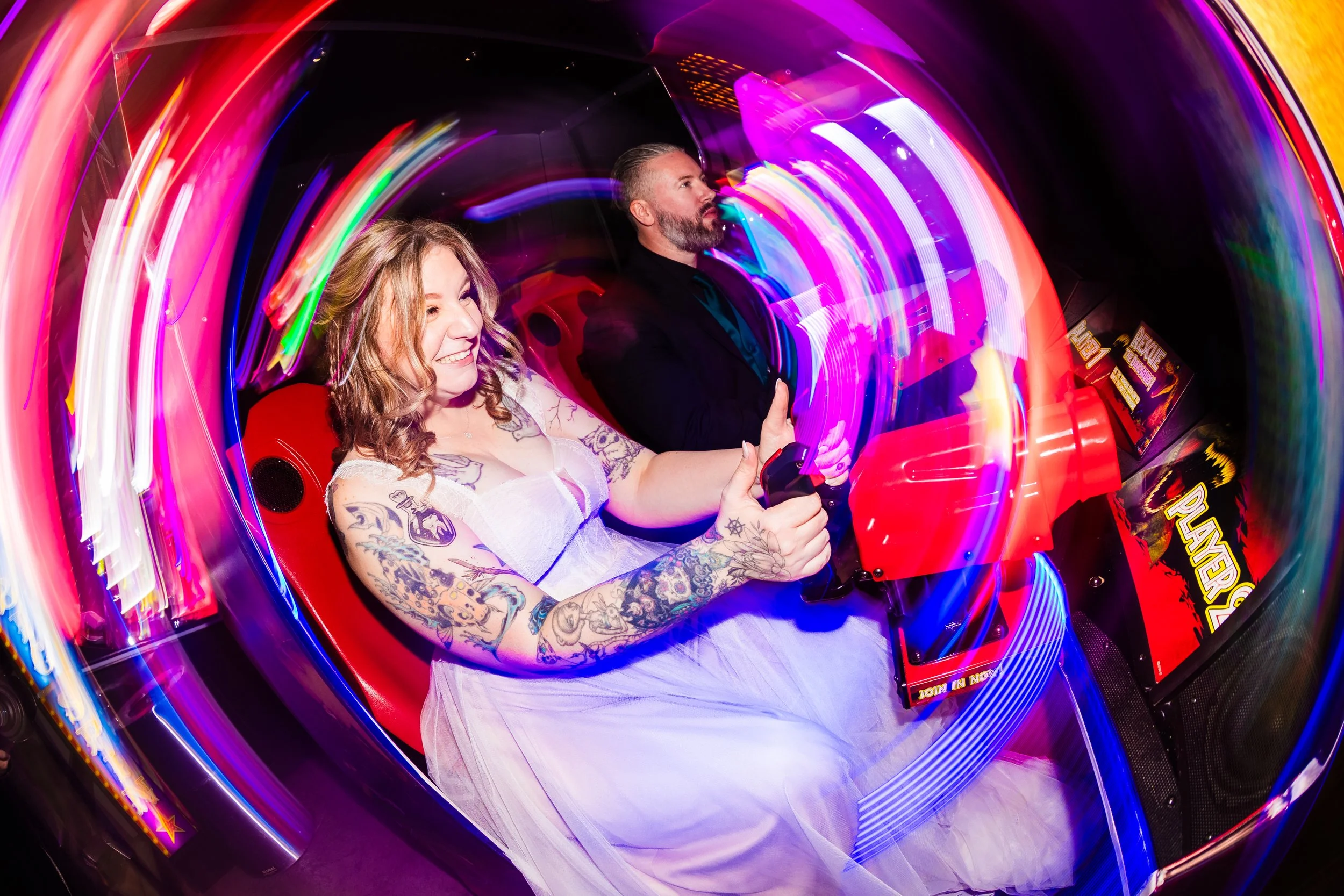 People playing a video game ride in an arcade with colorful neon lights.
