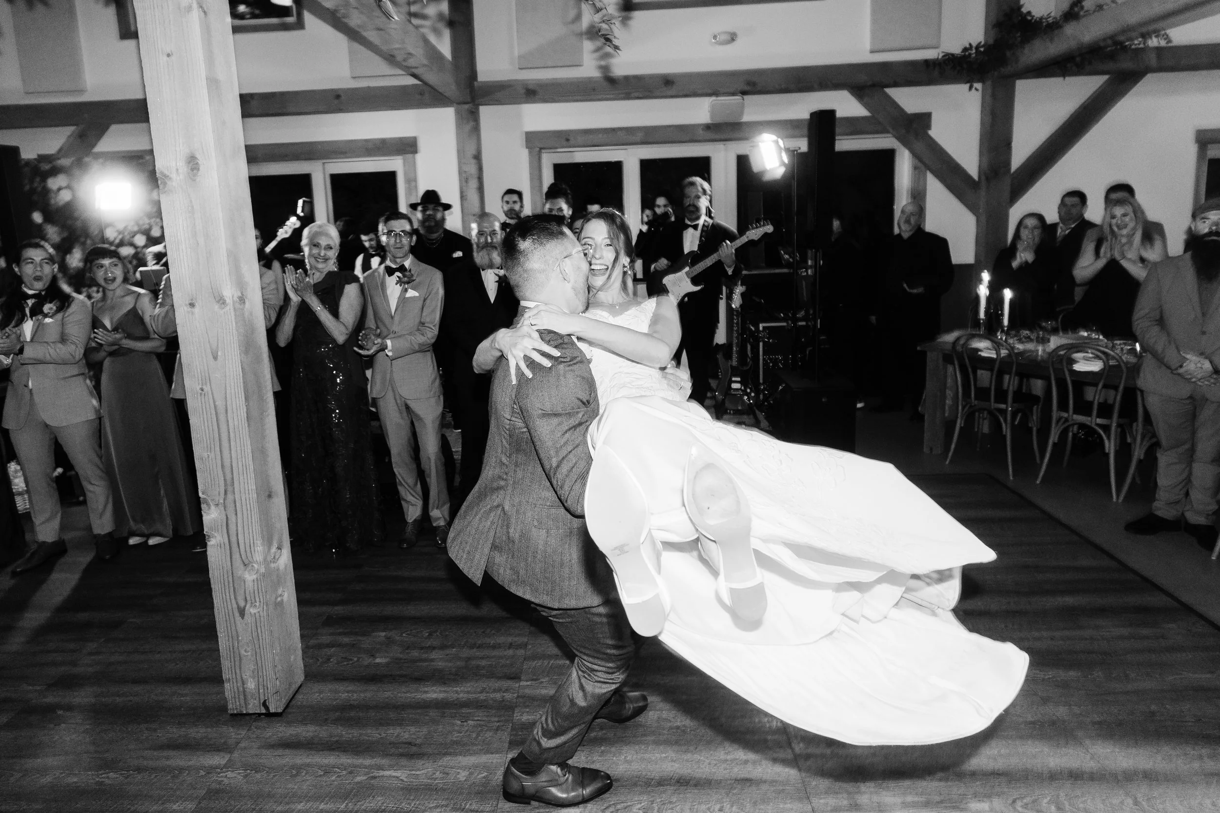 A newlywed couple dancing at their wedding reception with guests watching and smiling in the background.