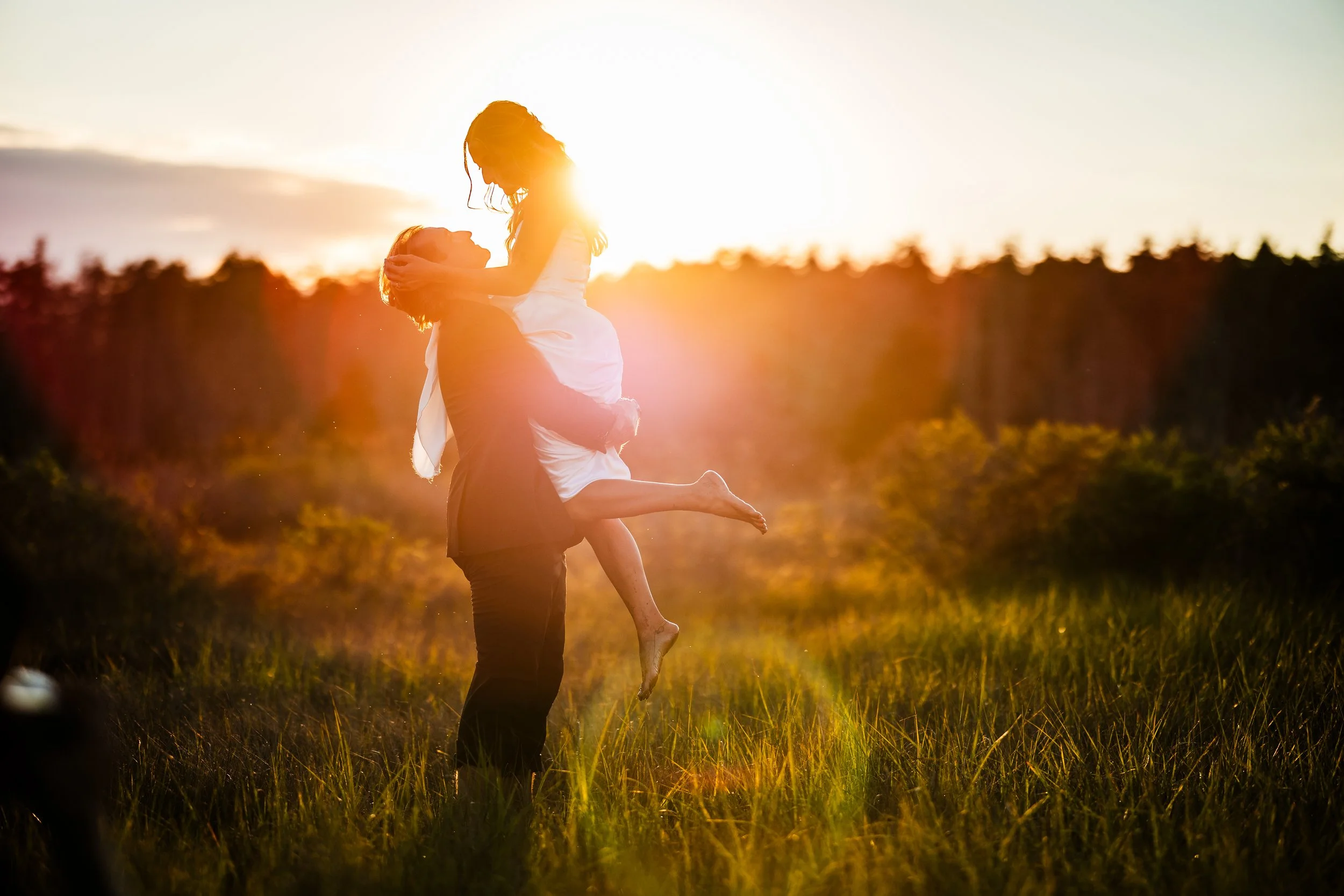 A couple enjoying each other outdoors during sunset, with the man lifting the woman in the air.