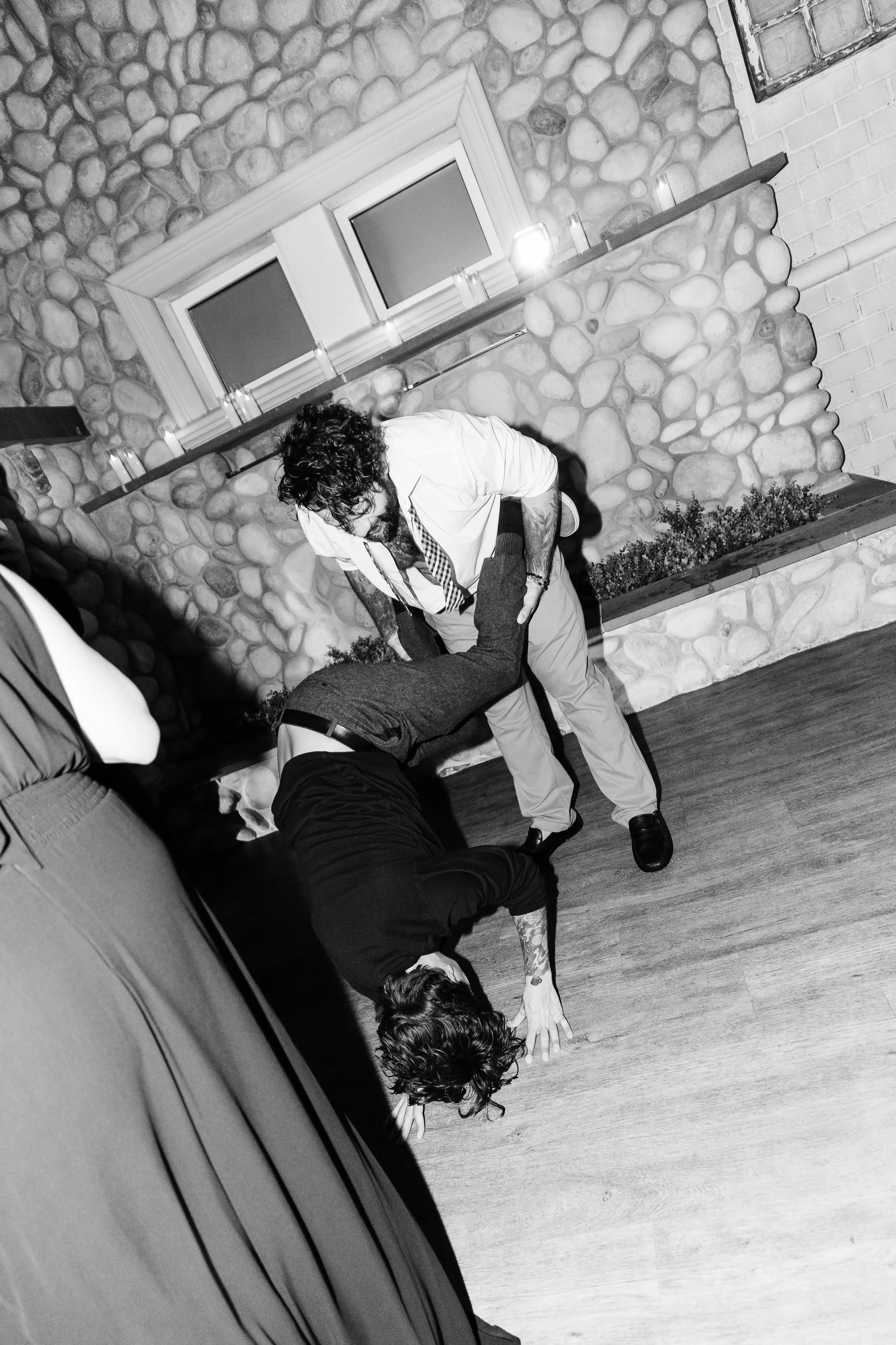 Two men fighting in a room with a stone wall and a window, one man on the ground and the other standing over him.