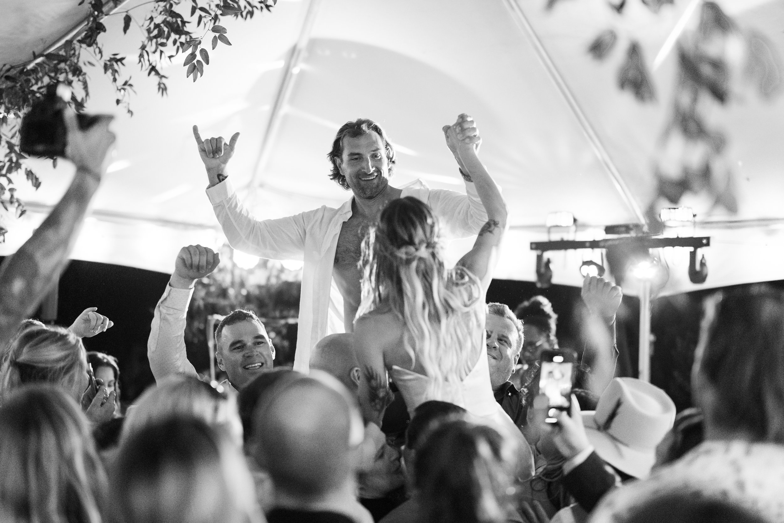 A group of people dancing and celebrating at an outdoor event under a canopy, with a man and woman enjoying the moment, black and white photo.