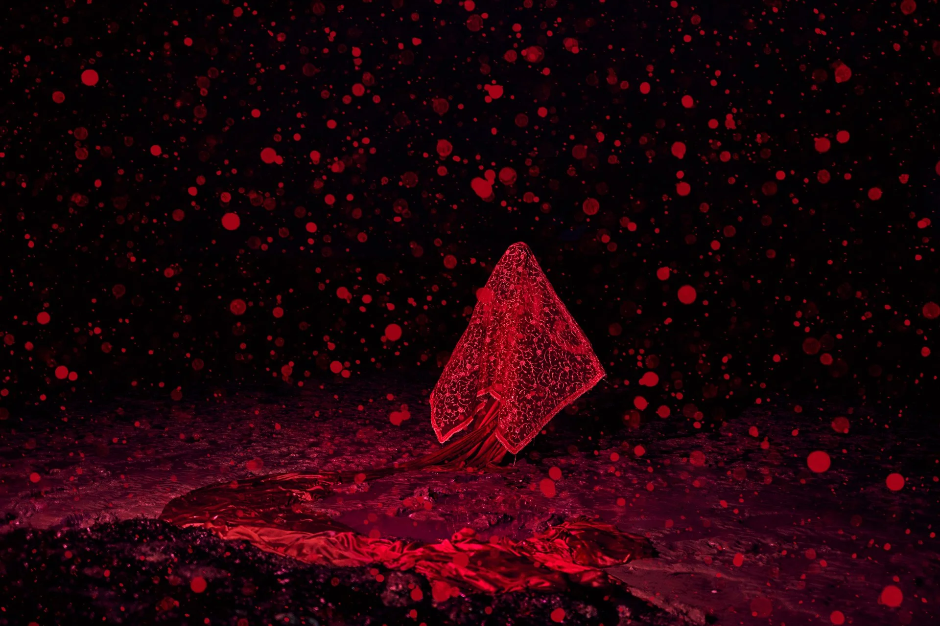 A red, ornate umbrella standing open on the ground with a dark background filled with red spray paint splatters.