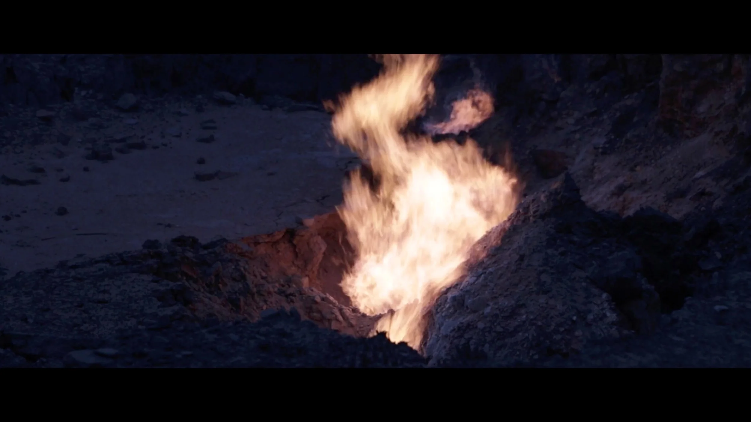 Lava flowing into a crater or volcanic vent, creating bright flames and smoke in a volcanic landscape.