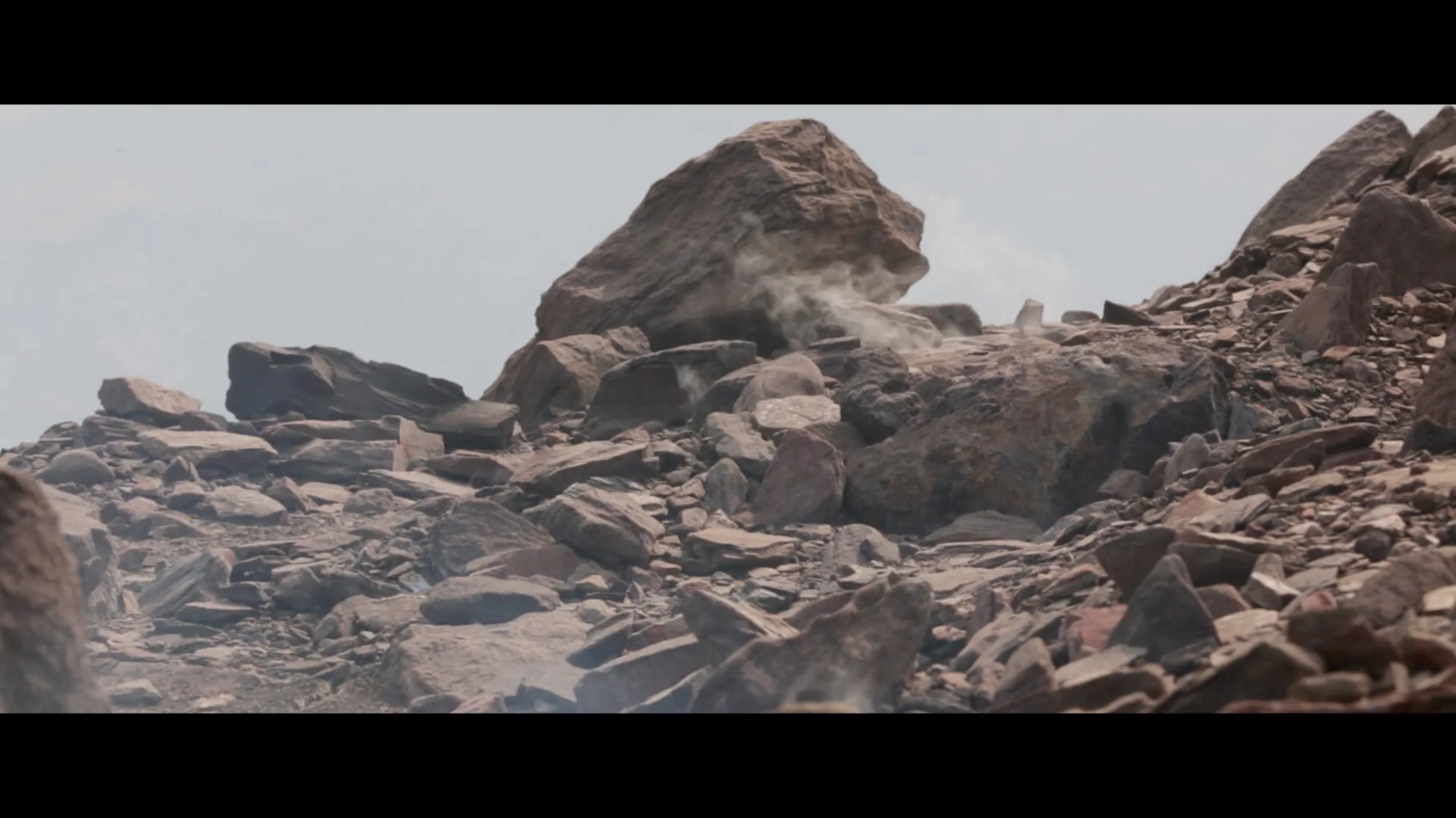 Rocks and boulders on a dry, rocky mountain or desert landscape with dust rising.