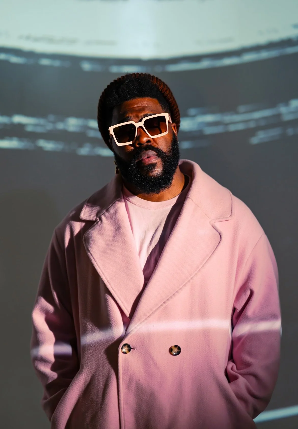 Person in a pink coat wearing sunglasses, standing against a blurred background.