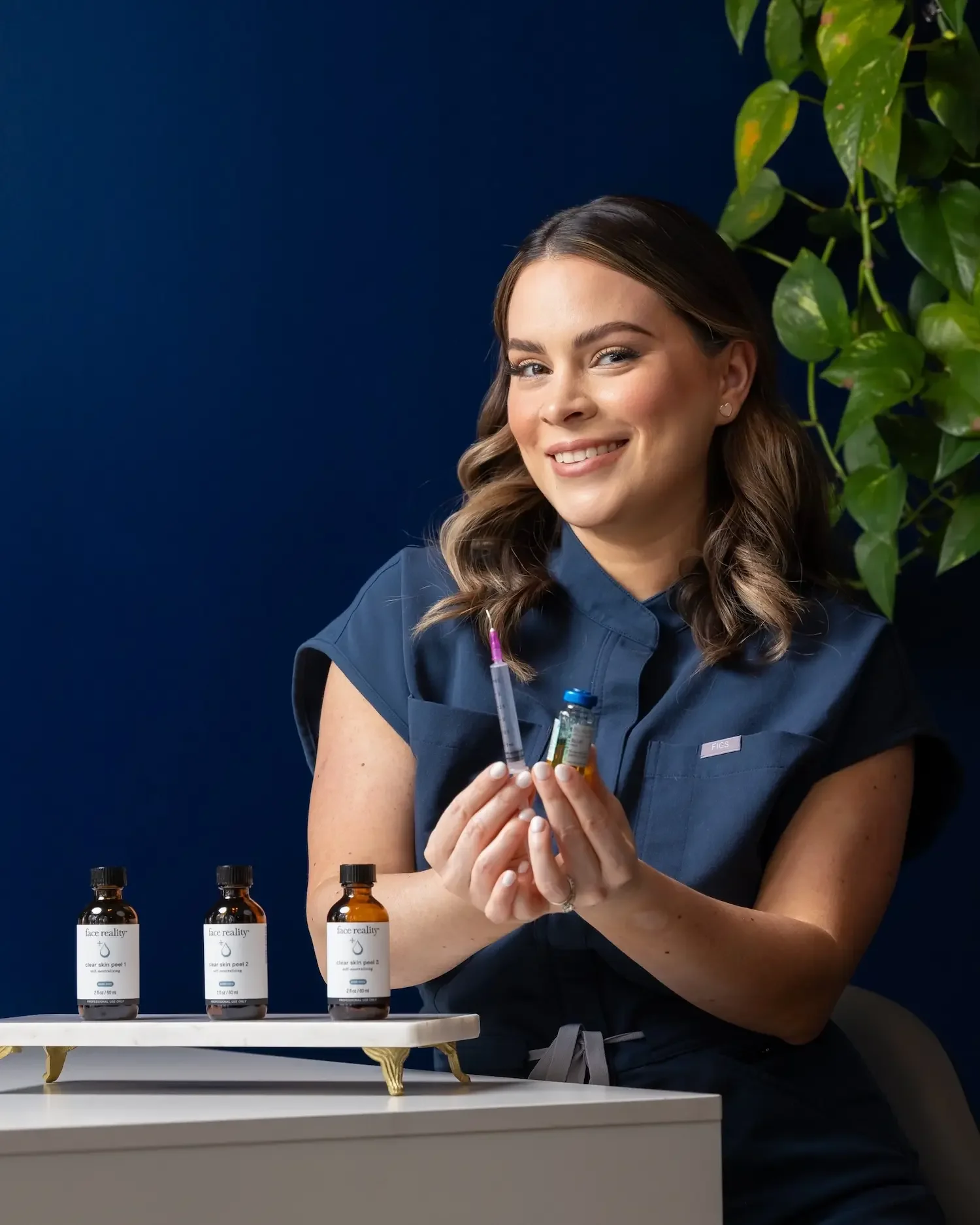 Yano Skincare esthetician holding a syringe and vial with Face Reality clear skin peel bottles displayed on a marble tray.