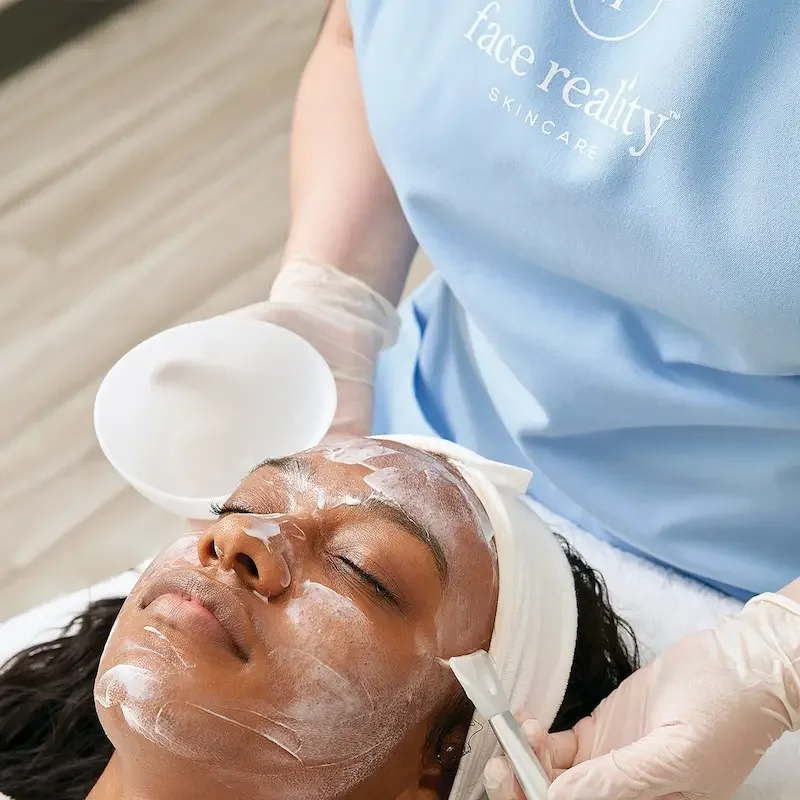 Esthetician applying Face Reality Skincare acne treatment mask to a client's face during an Acne Bootcamp session.