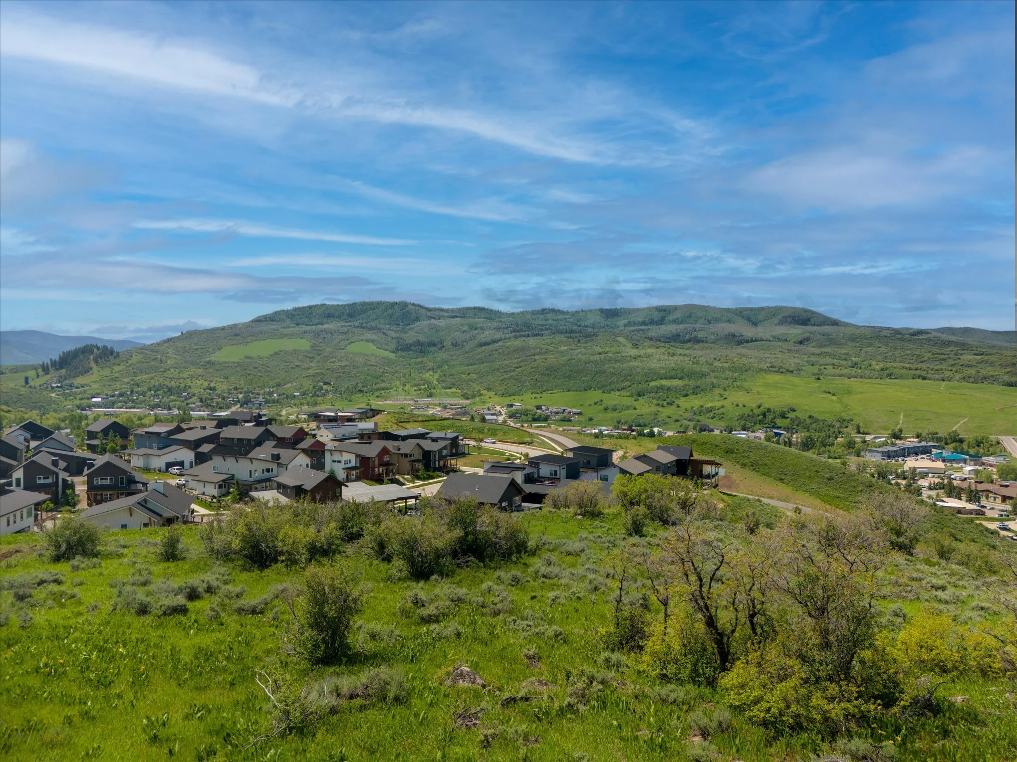 Suburban neighborhood with houses and green hills in the background under blue sky.