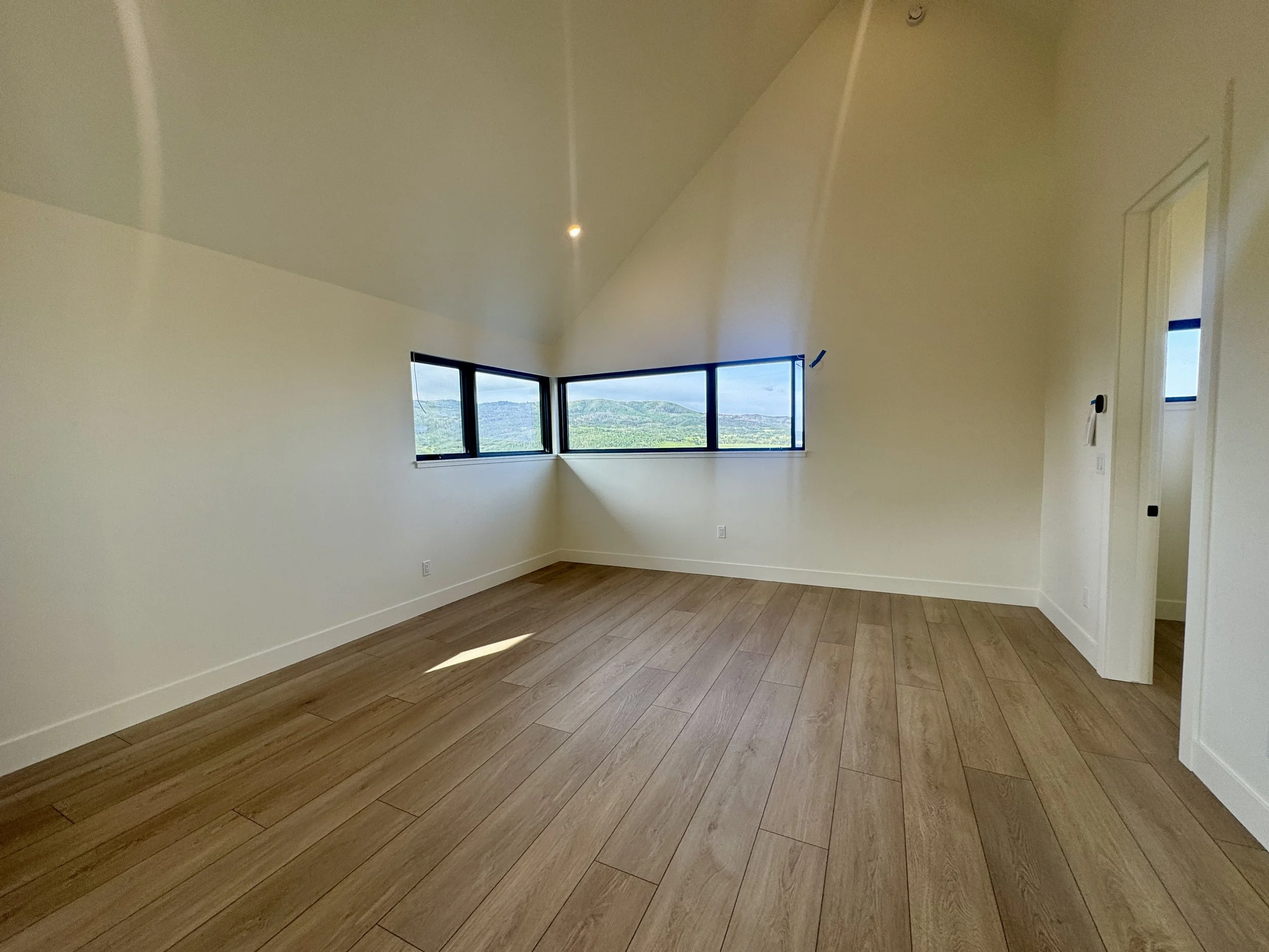 Empty room with wooden floor, white walls, large windows, and a sloped ceiling.