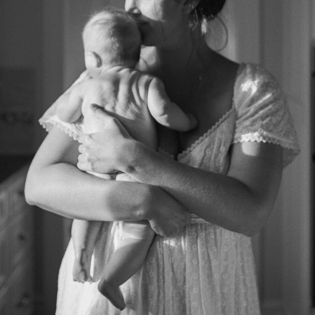 Greensboro family photography session with a mother cuddling her baby in natural light. Documented on 35mm film in North Carolina.