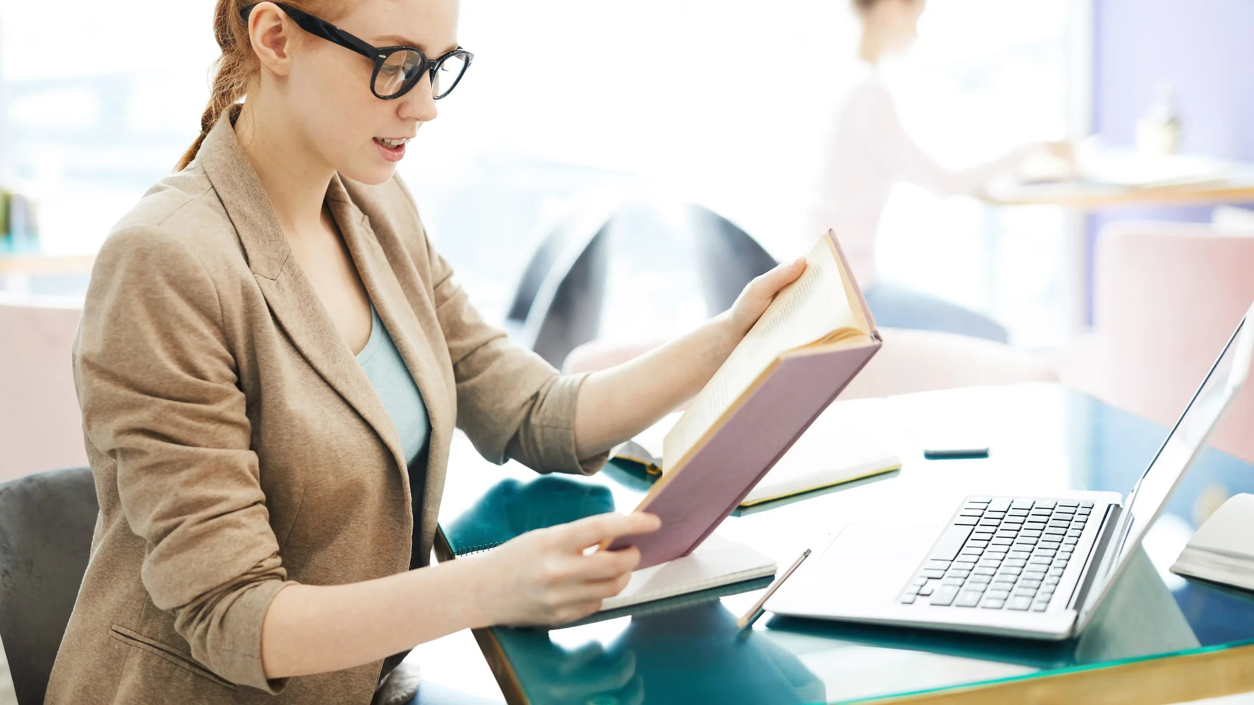 A young woman in glasses studies an open book while doing her homework for online therapy in Greenacres, Florida.