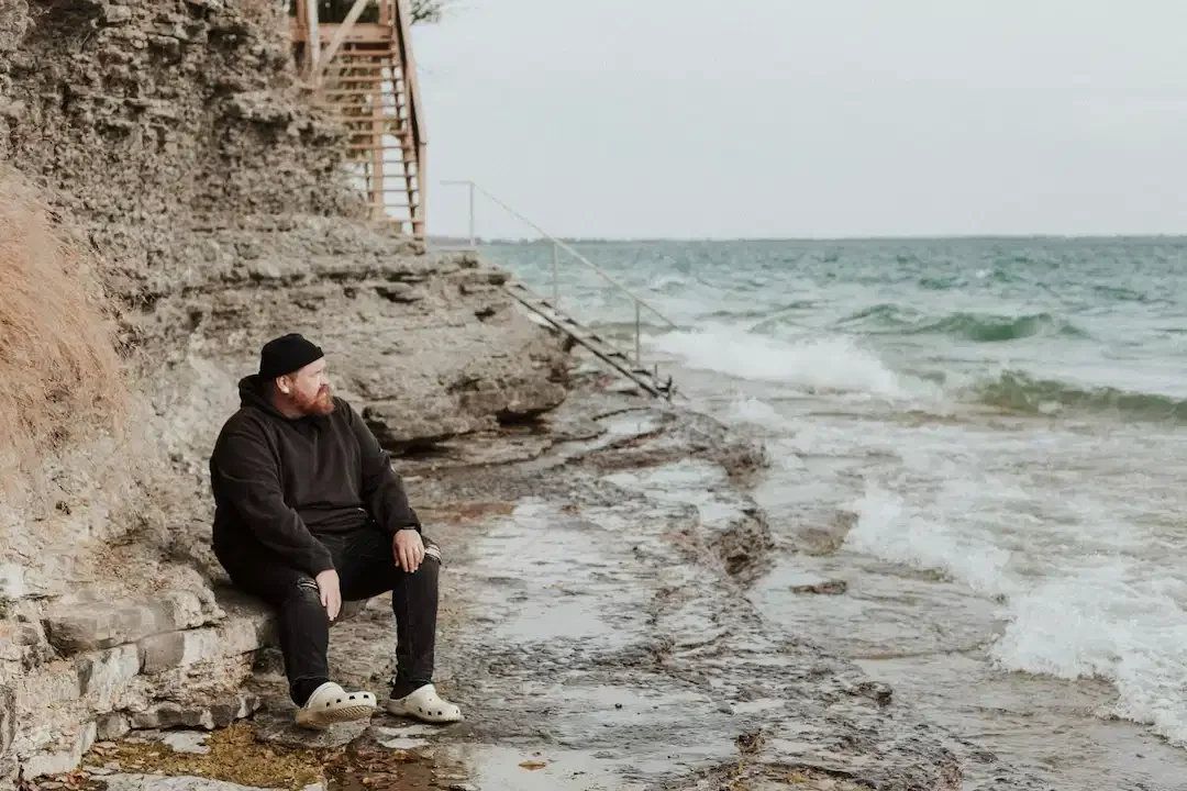 Bearded man sits at the beach alone and anxious, isolating himself from help.