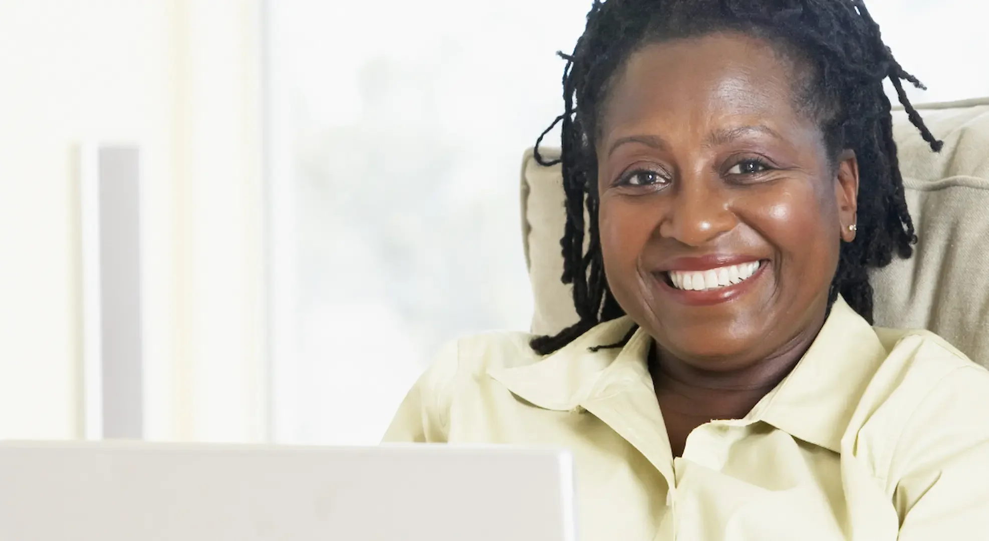 A professional woman looks up from a laptop smiling while she enjoys online therapy