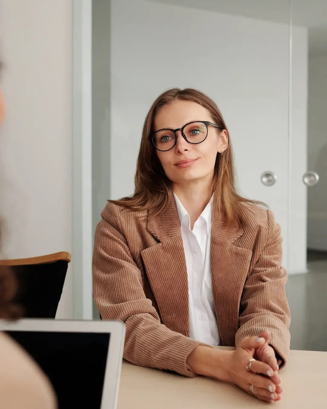 A professional woman in her lates 20s sits at a desk ready to talk about her sobriety with the person across from her.