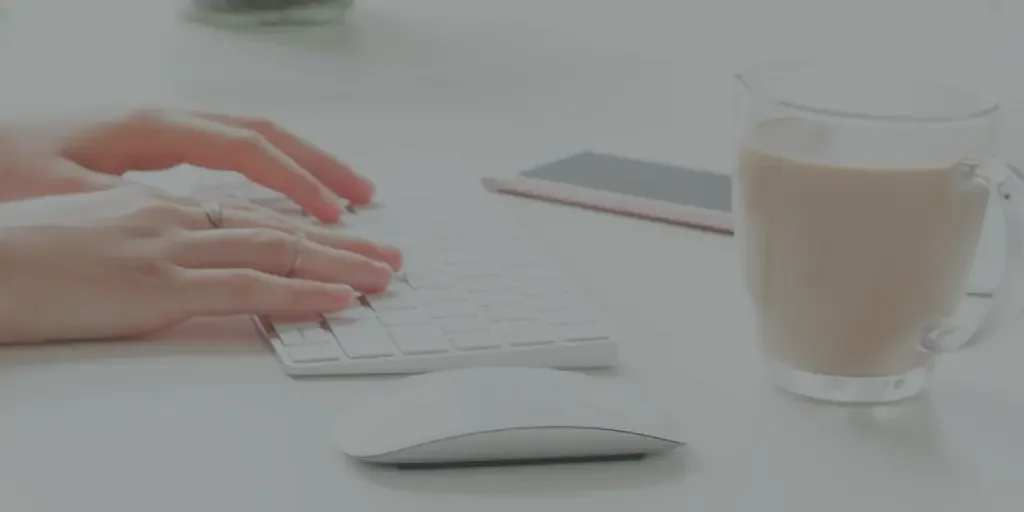 A woman's hands rest on a keyboard in front of a computer, cell phone, and cup of coffee as she begins the instructional design process.