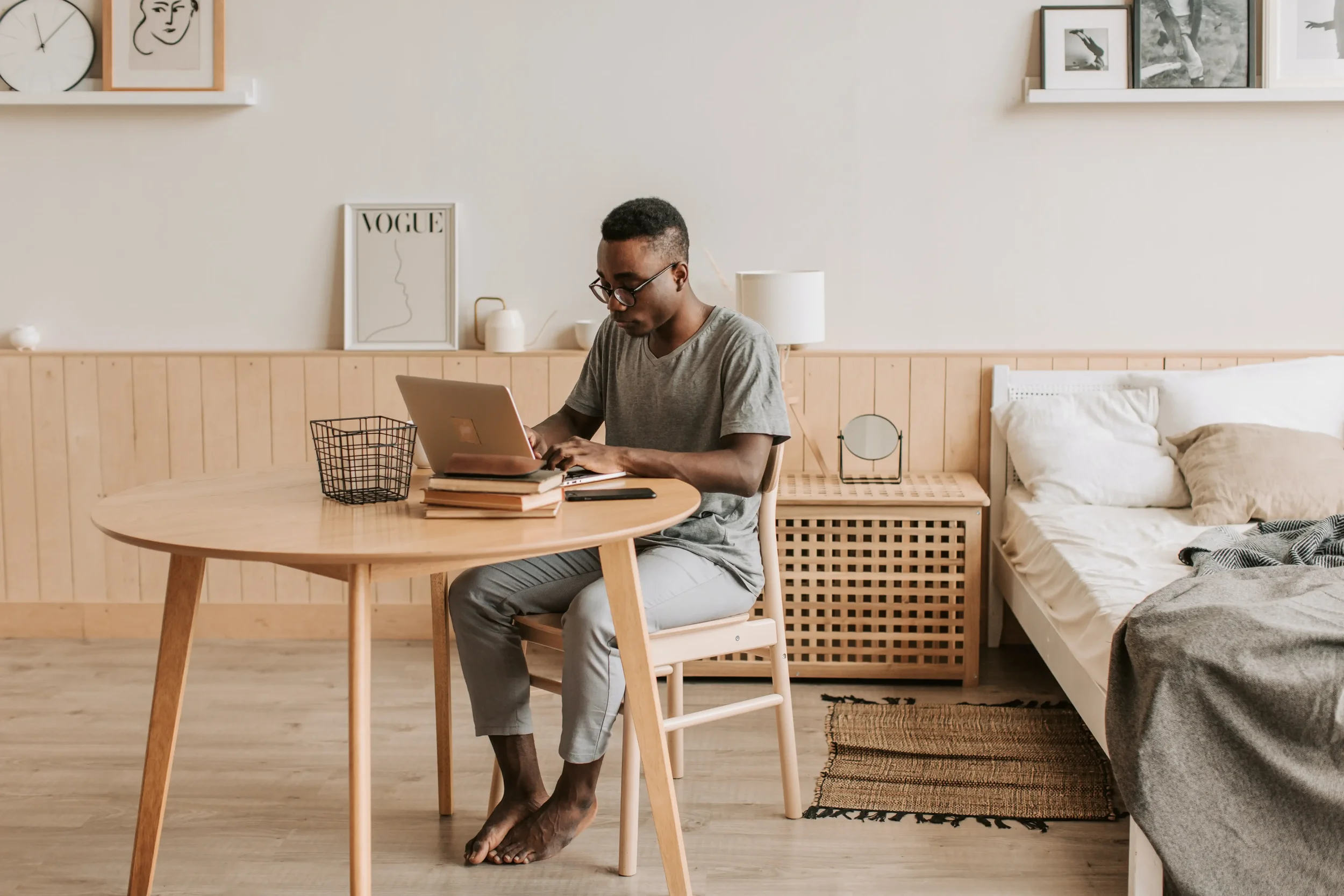 A person in a grey shirt sitting at a wooden table, focused on a laptop in a bright, minimalist room, symbolizing the quiet study and intentionality of personal growth.