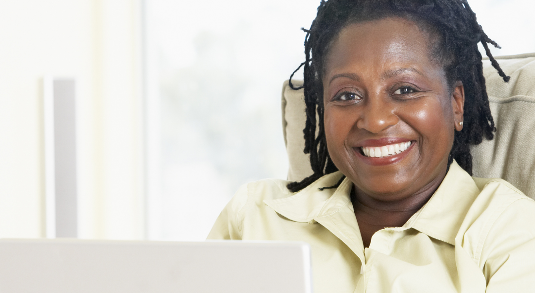 A professional Black woman looks up from a laptop smiling while she enjoys online therapy