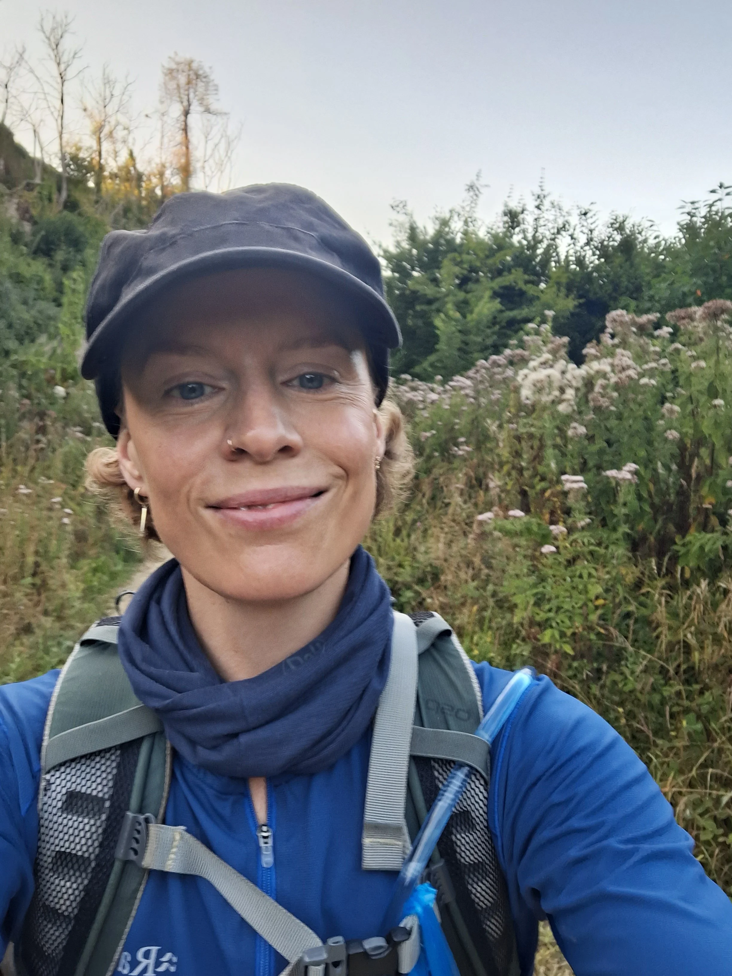 A smiling woman in a cap and sportswear, standing in a field of flowers at dusk