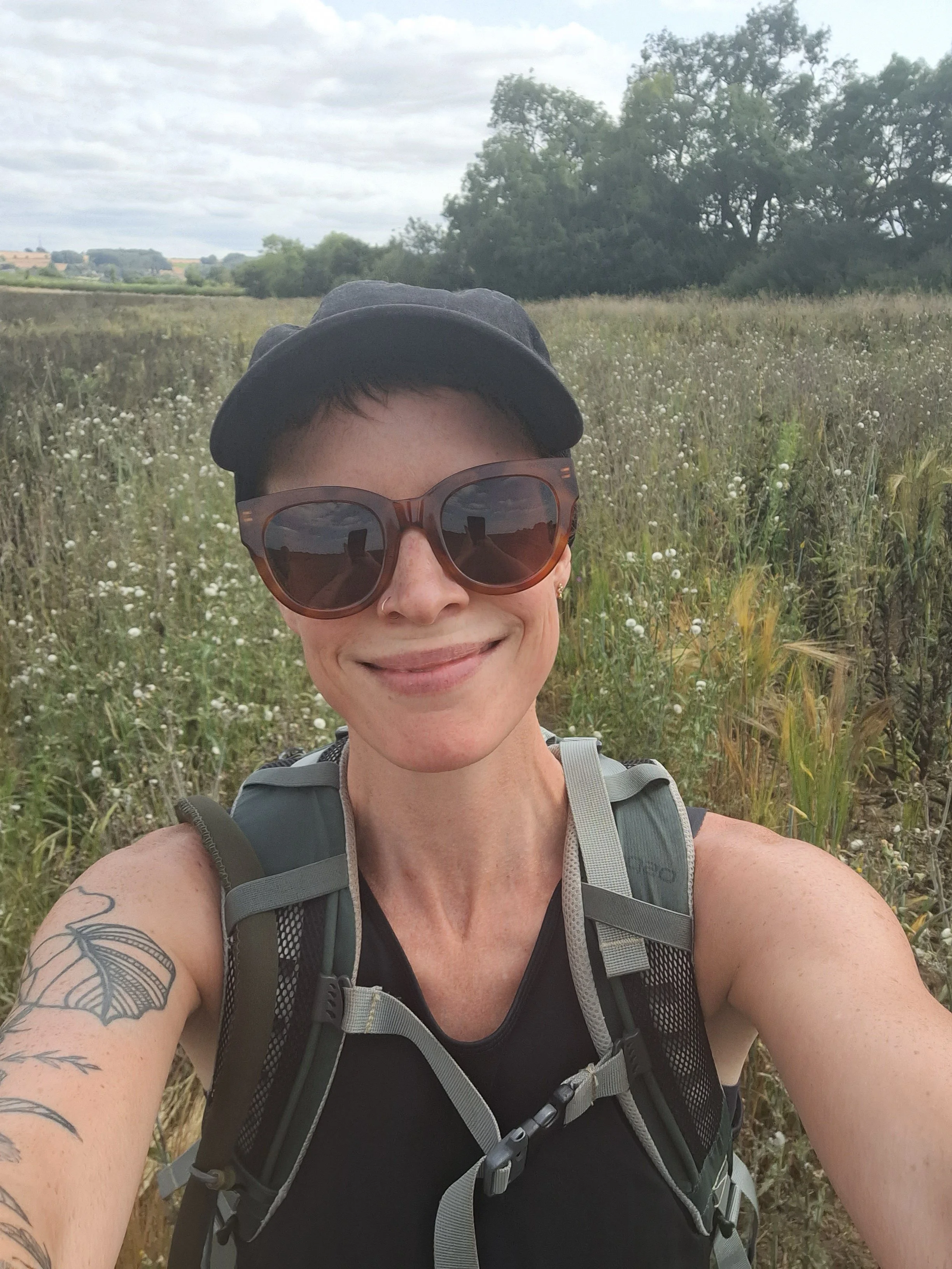 A smiling woman in sportswear, cap and sunglasses taking a selfie in a field full of flowers