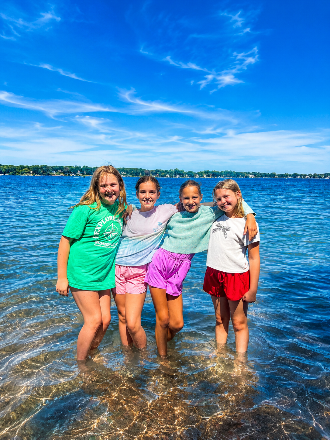 Four middle school girls laughing together in a lake during a summer mindfulness and wellness camp in Mounds View MN