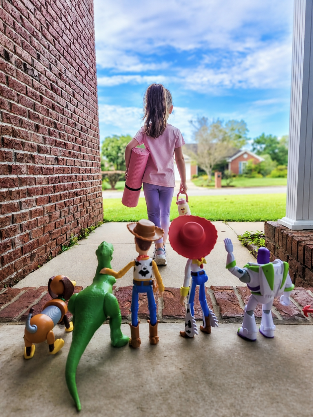 Girl walking out the door with a yoga mat and water bottle, surrounded by classic toy figures — imagery for Imagination Takes Flight™ kids yoga camp in New Brighton, Minnesota
