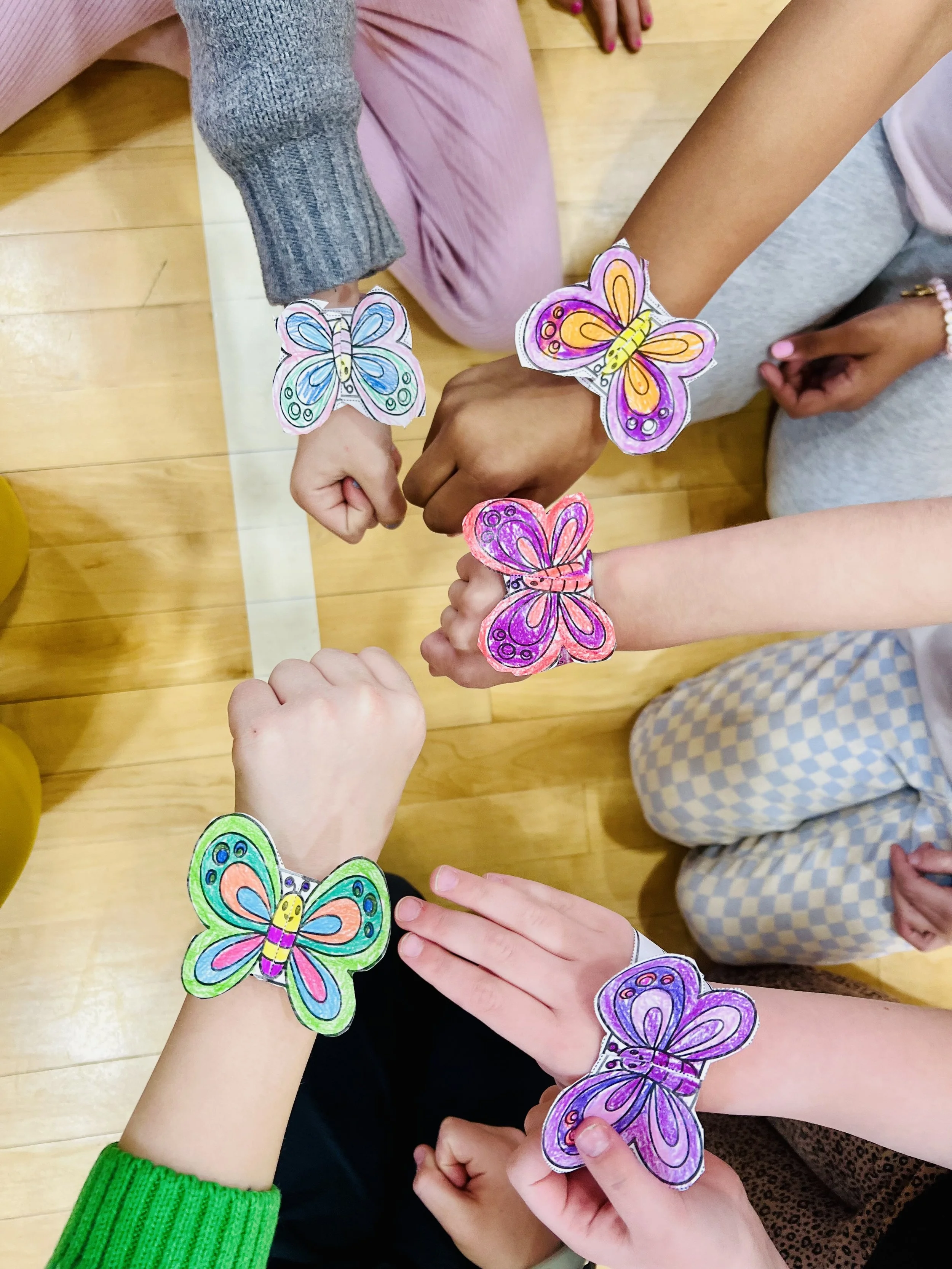 Elementary students at a Roseville MN non-school day yoga camp showing butterfly craft bracelets during mindfulness retreat