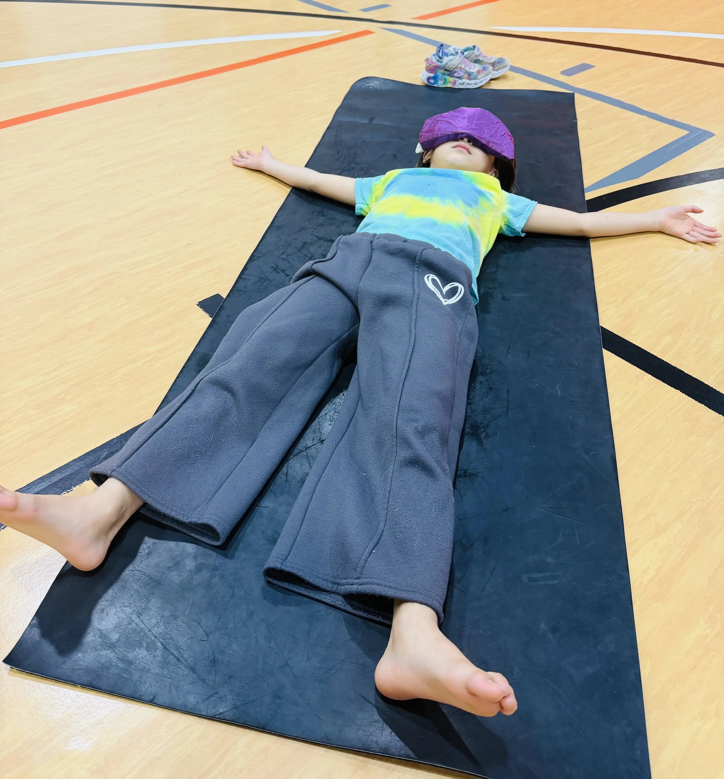 Child resting with eye pillow during mindfulness relaxation activity in Mounds View MN kids yoga program