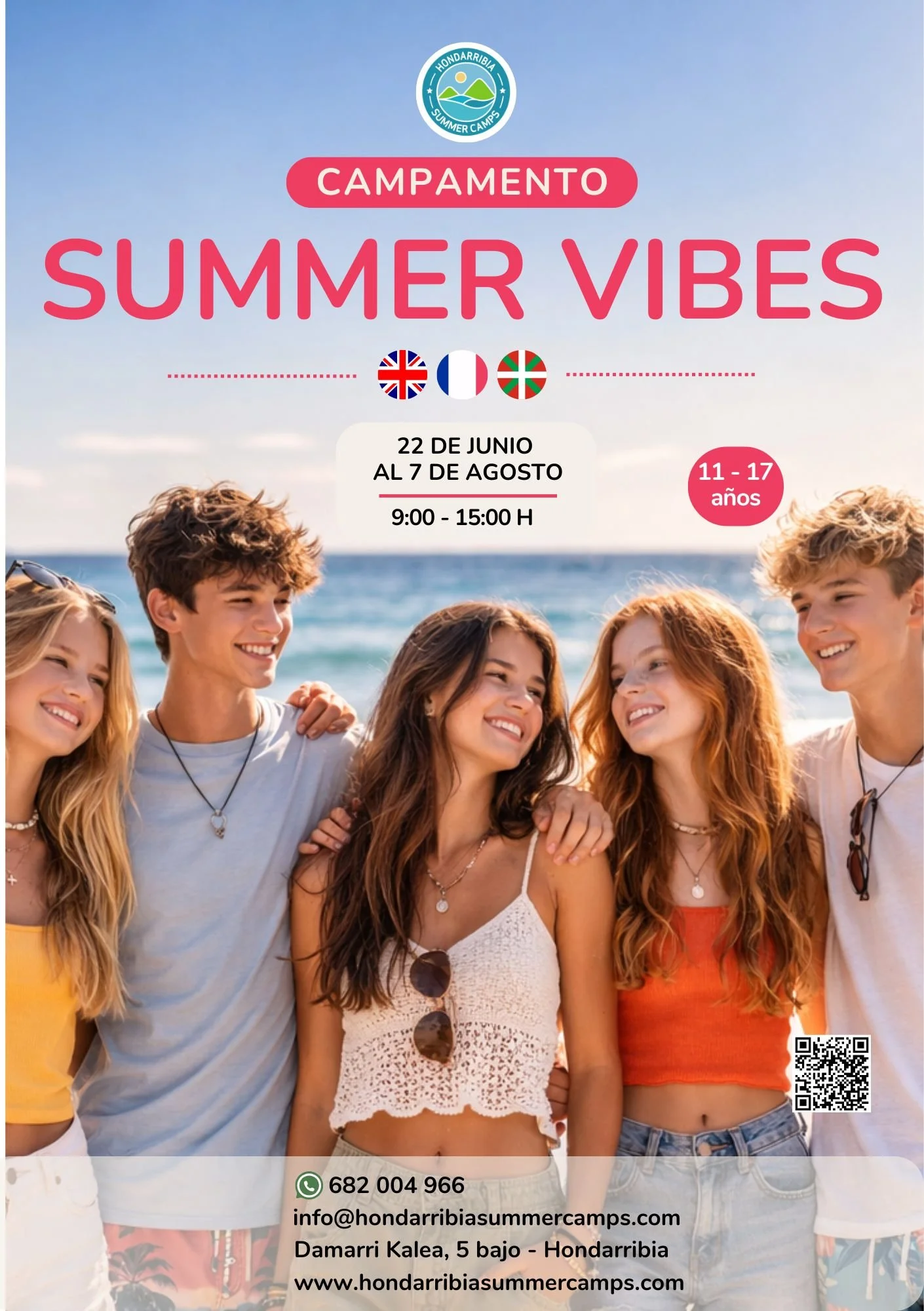 Grupo de jóvenes sonriendo en la playa durante un campamento de verano en Hondarribia, con fondo de mar y cielo azul.
