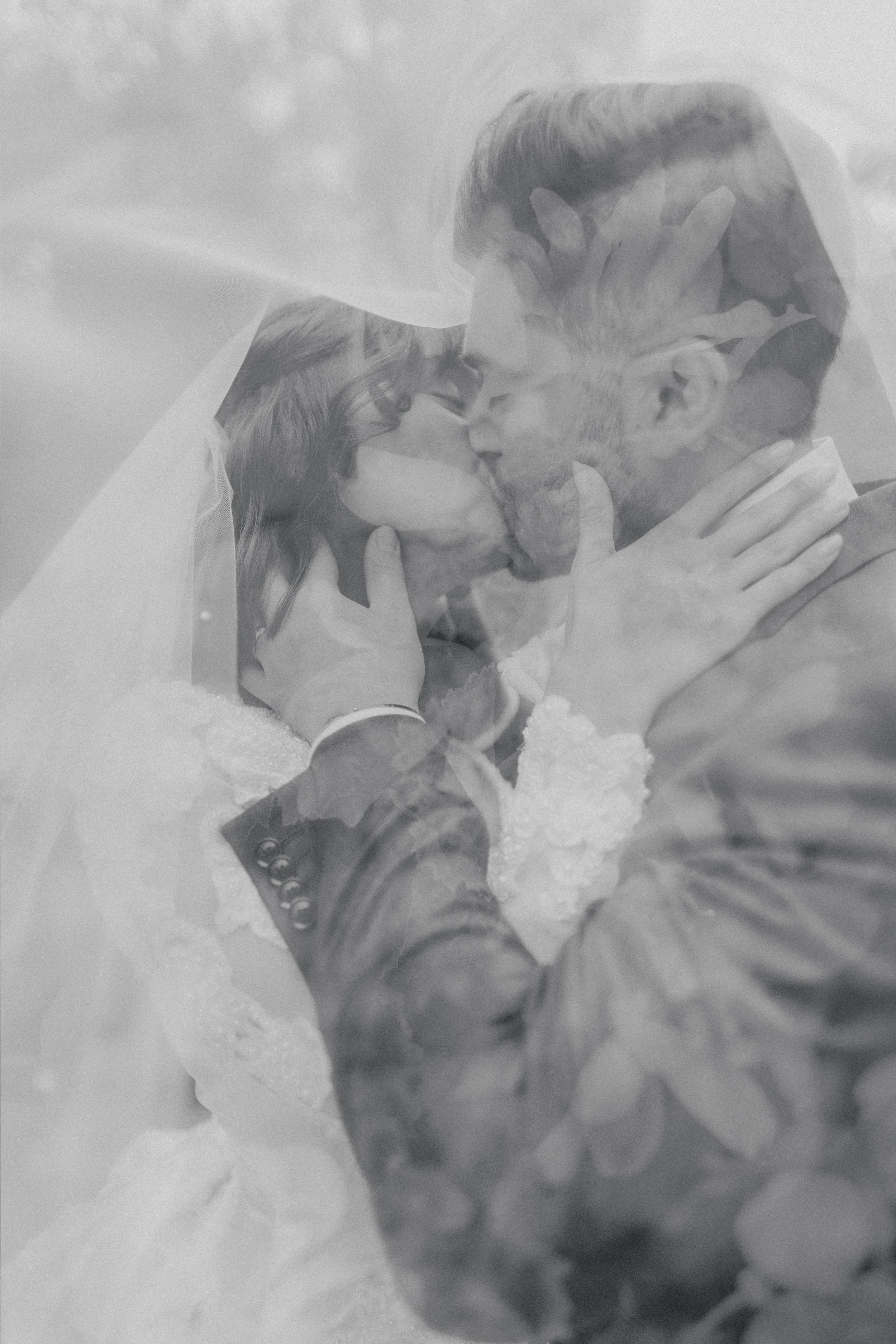 A black and white photo of a bride and groom kissing, with the image taken through a reflective surface or overlay.
