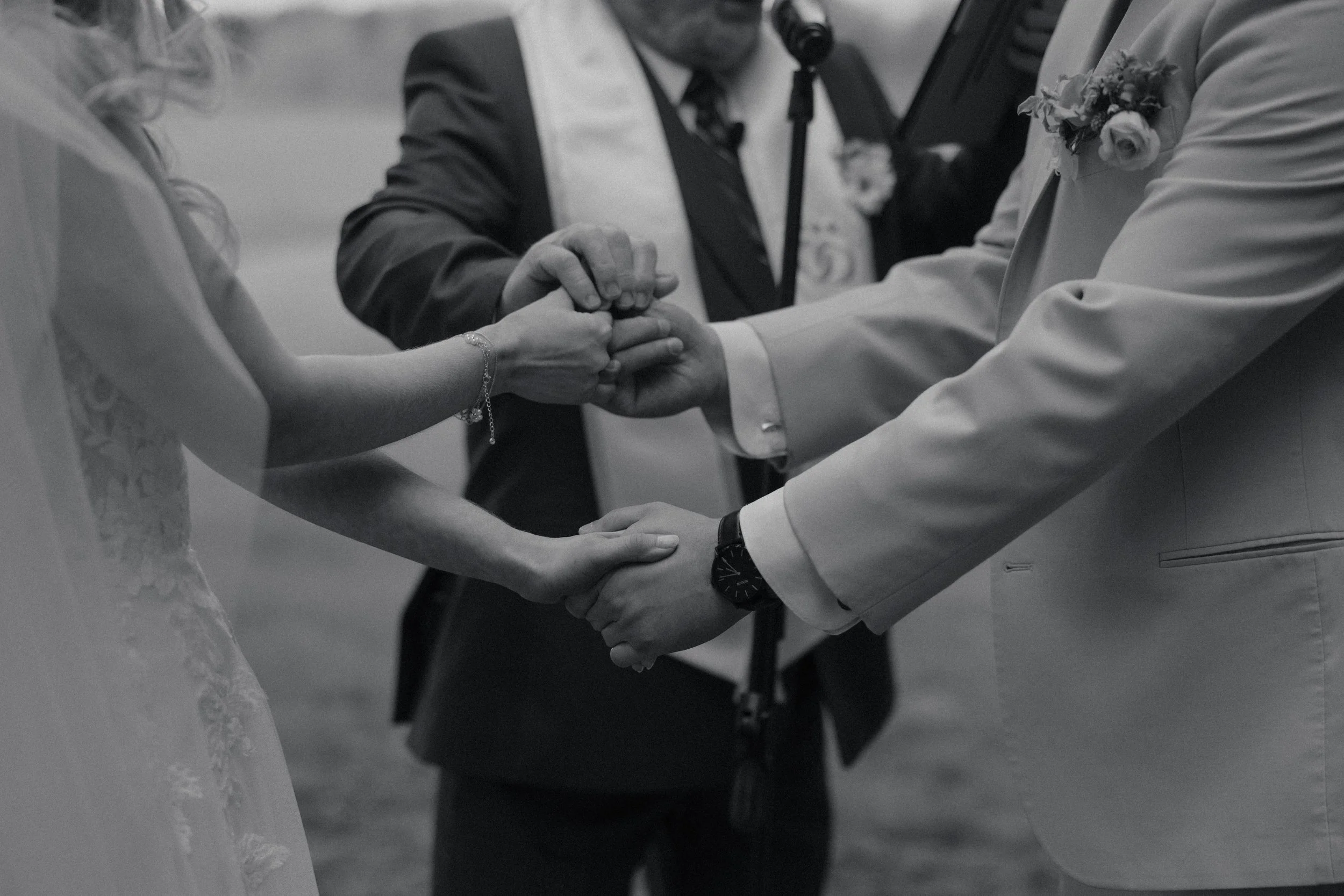 A couple holding hands during their wedding ceremony, with an officiant in the background.