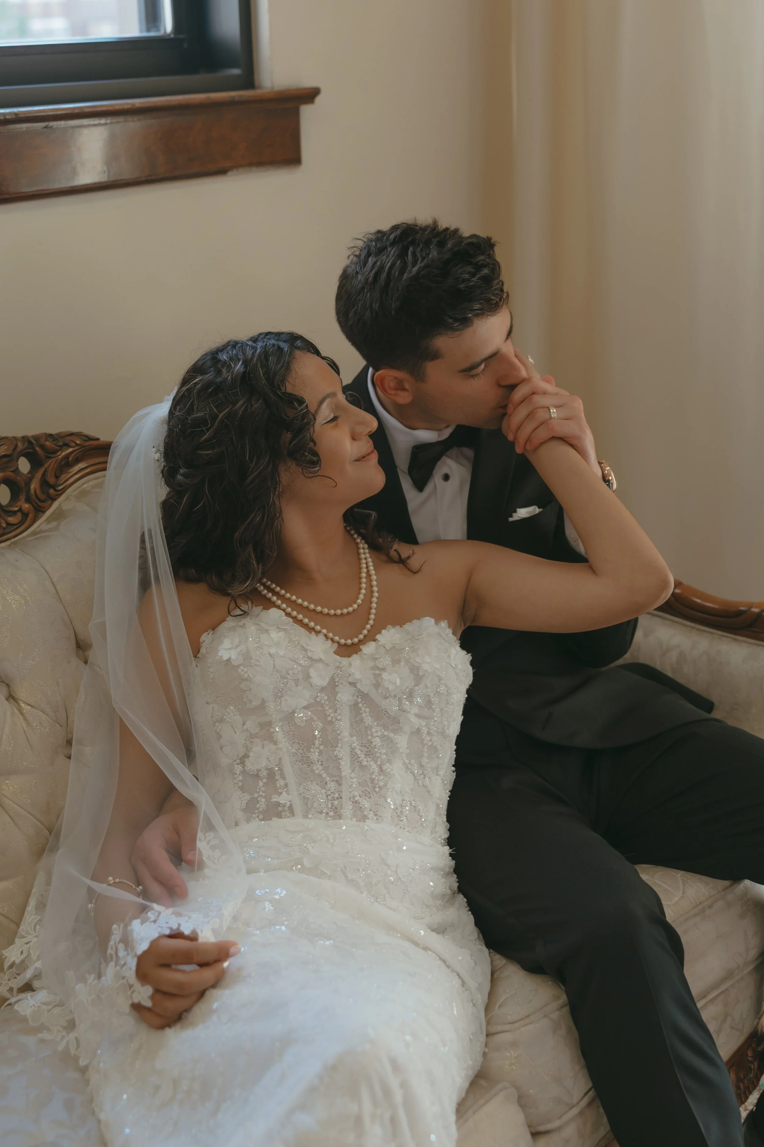Couple sitting on couch, groom kissing brides hand at the Treasury in Pontiac Michigan