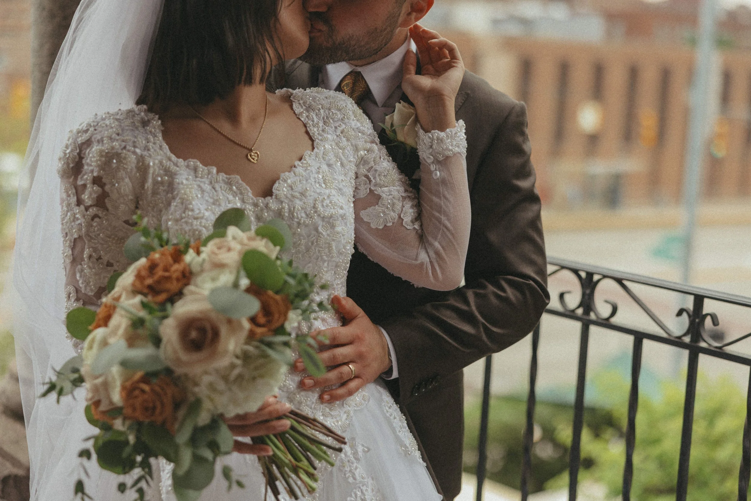 A bride and groom sharing a kiss during their wedding, with the bride holding a bouquet of white and peach flowers, both dressed in wedding attire.