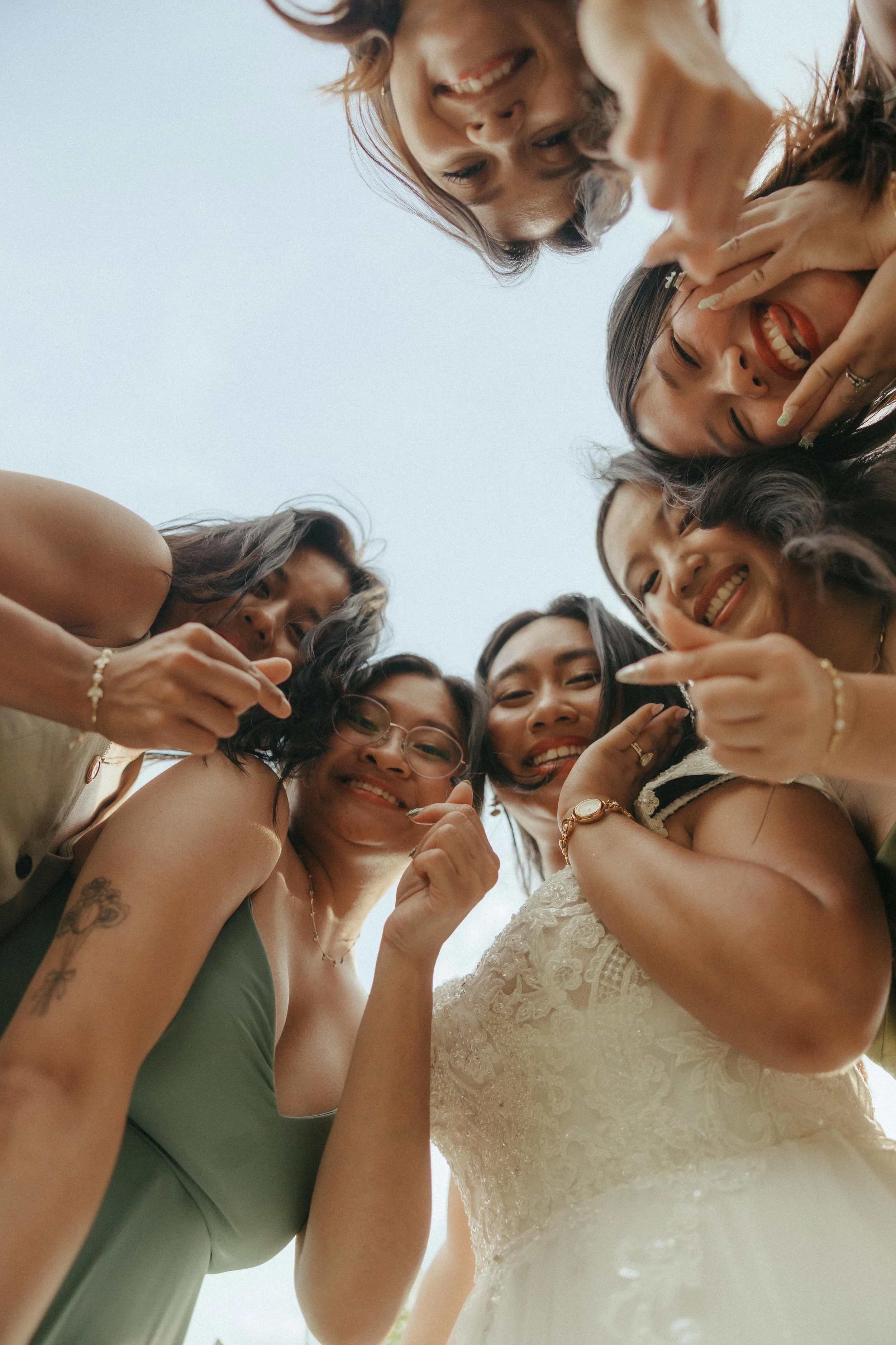 Group of women smiling and making heart gestures, seen from below against a clear sky.