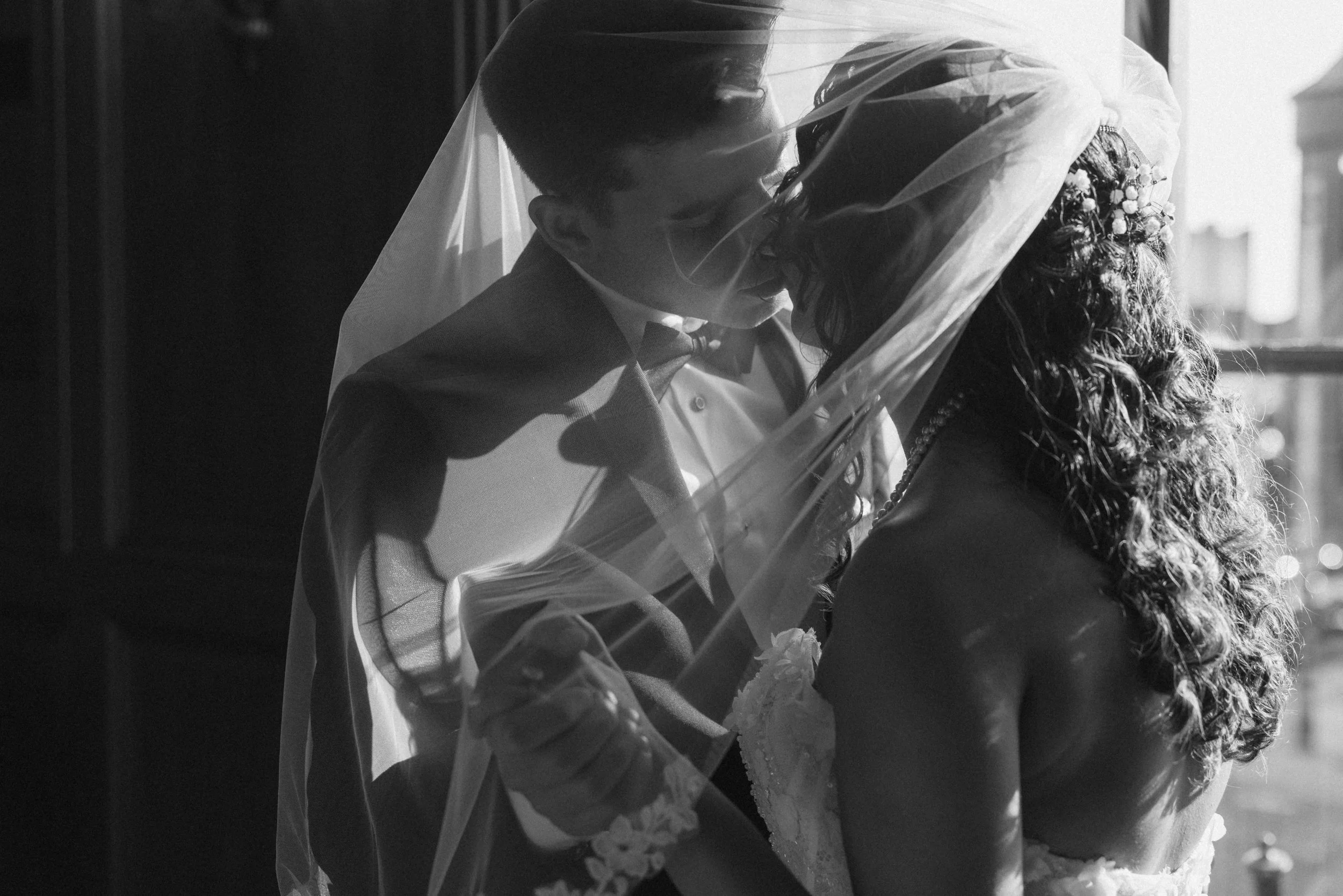 Bride and groom under veil holding hands and kissing