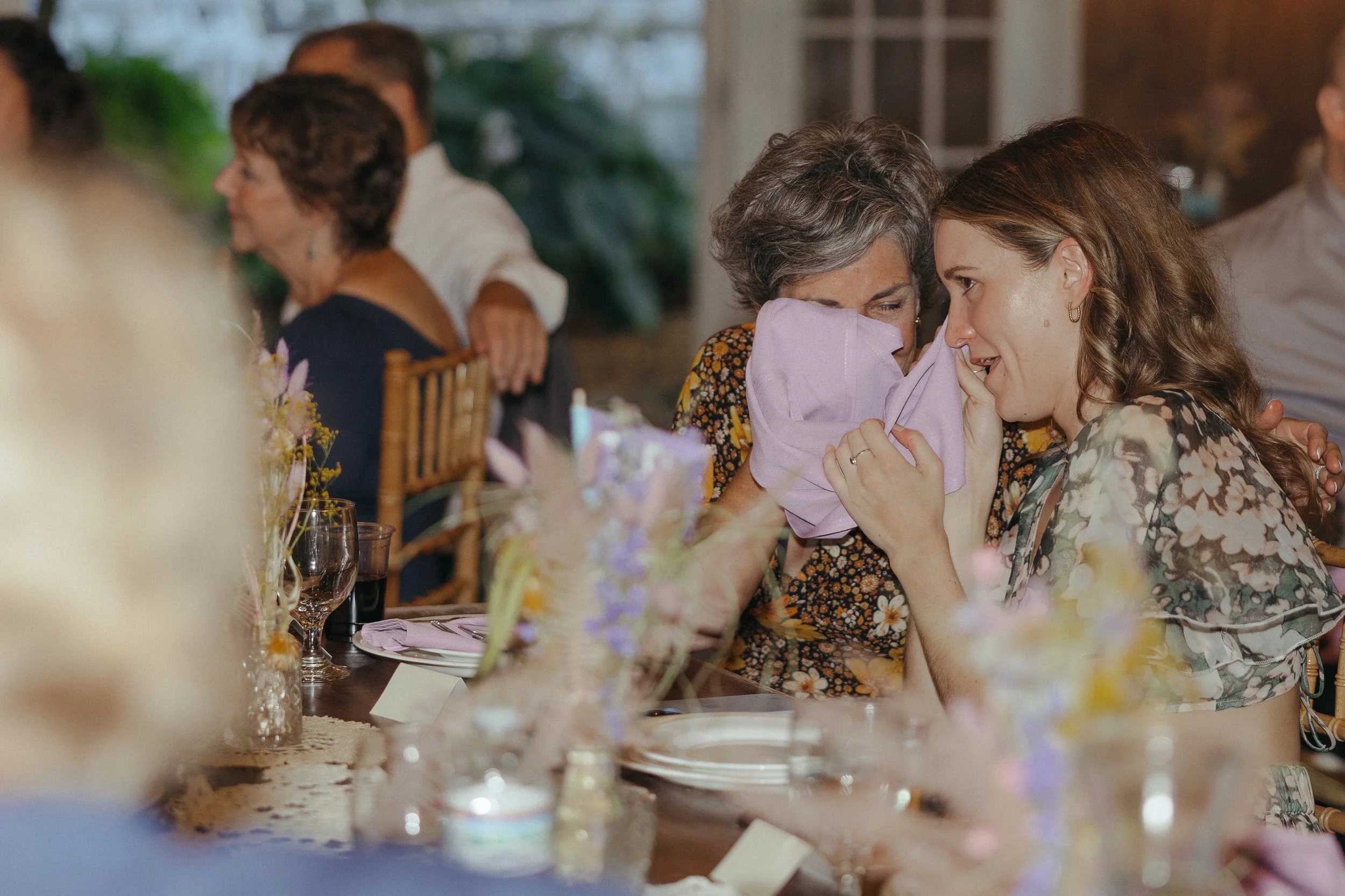 Candid of people sitting at a dining table, with two women wiping tears during wedding reception speeches at MillCreek Wilde, in Van Buren County, Michigan