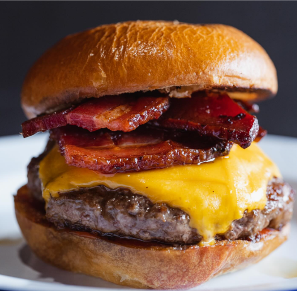 Close-up of a cheeseburger with bacon, melted cheddar cheese, a hamburger patty, bacon strips, and a sandwich bun.