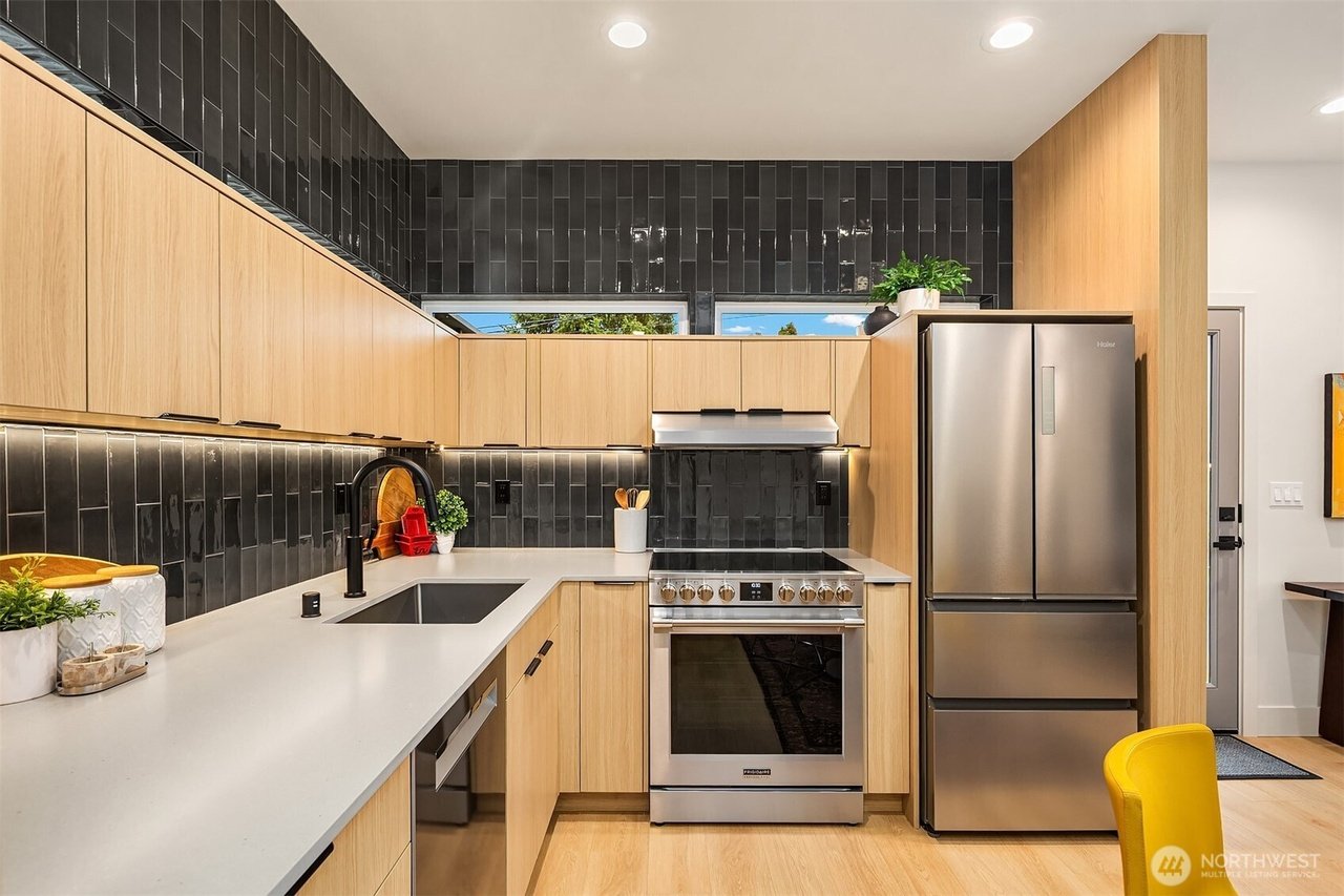 Modern kitchen with light wood cabinets, dark tile backsplash, stainless steel appliances, and white countertops.