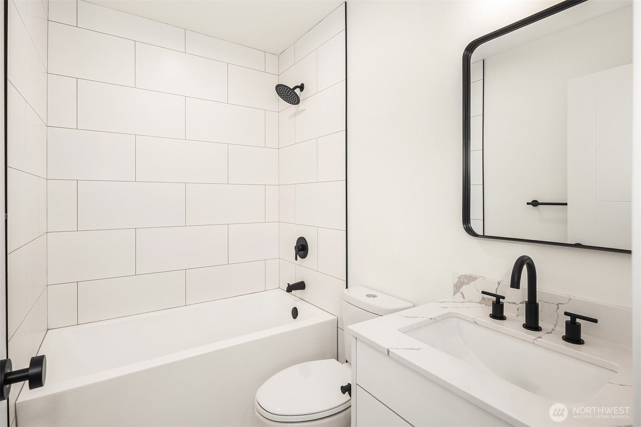 Modern bathroom with white tiled shower, black fixtures, a white vanity with marble countertop, and a rectangular mirror with black frame.