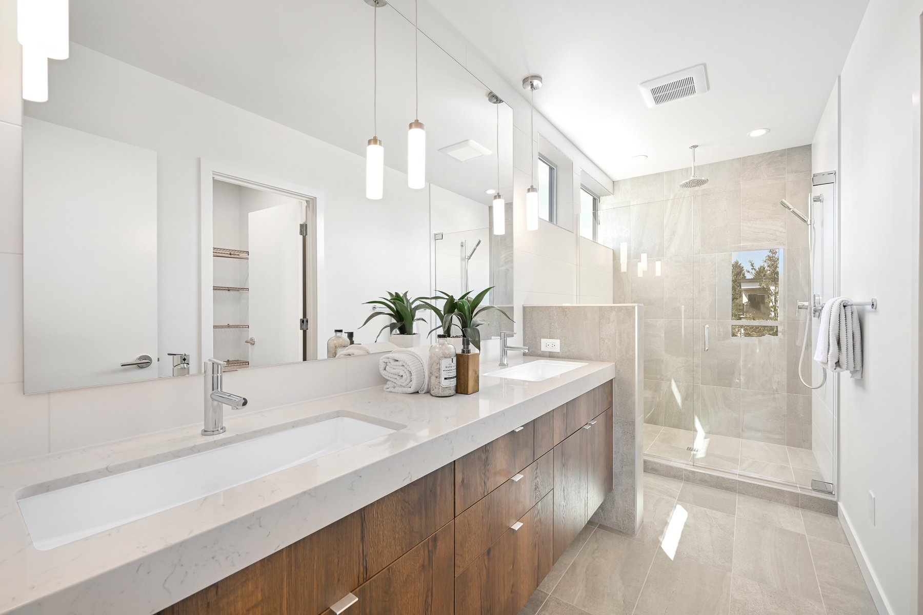 Modern bathroom with dual sinks, wooden cabinets, large mirror, and glass-enclosed shower.