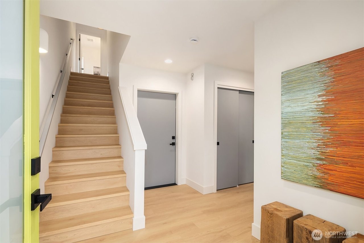 Modern interior hallway with light wood flooring, a staircase with wooden steps, grey doors, and contemporary artwork on the wall.