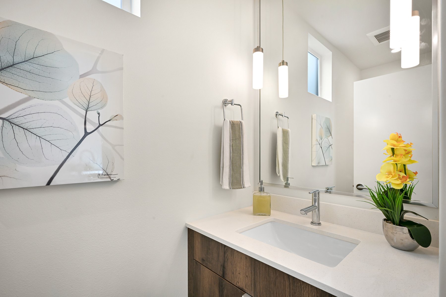 modern bathroom with sink, wooden vanity, large mirror, potted plant, framed leaf art, and pendant lights