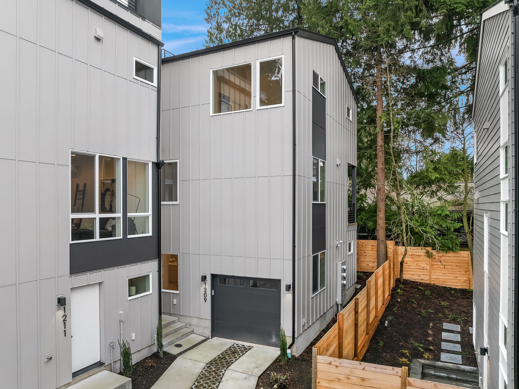 Modern row houses with gray siding, large windows, and adjacent fencing.