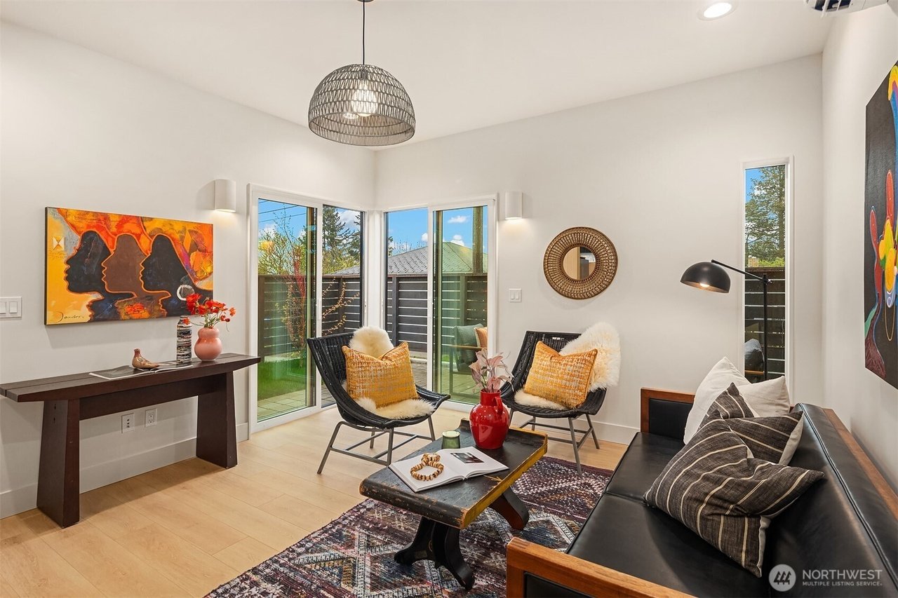 Modern living room with a contemporary design, featuring two black lounge chairs with yellow cushions, a black leather sofa with striped pillows, and a rustic wooden coffee table. Art on the walls, including colorful and abstract paintings, and a rat