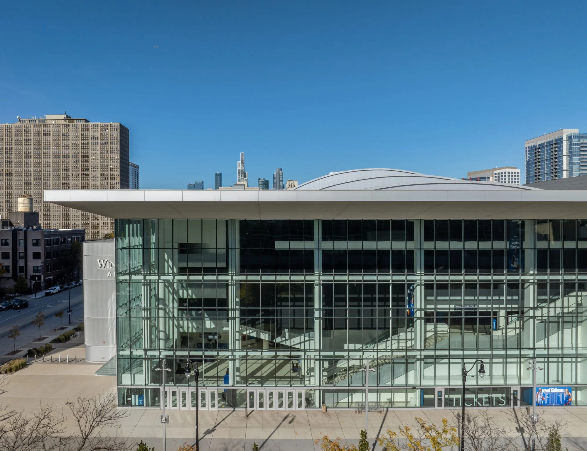 Modern arena glass building with surrounding cityscape and blue sky.