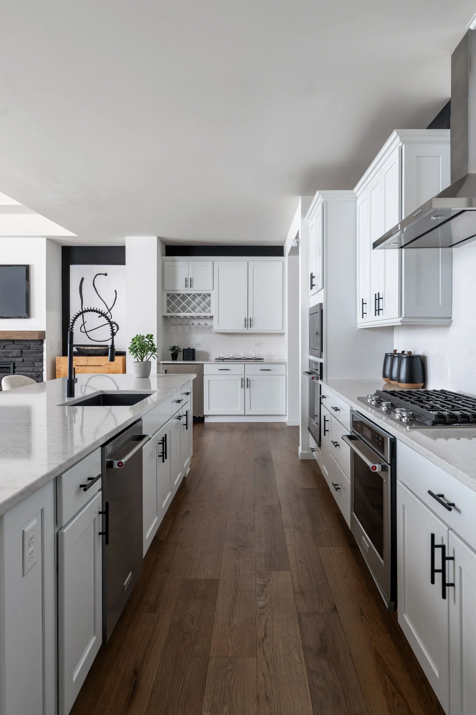 Modern kitchen with white cabinets, wood flooring, stainless steel appliances, black hardware, and a black faucet over the sink.