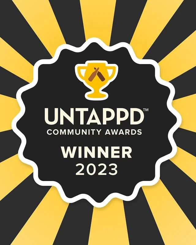 Award badge for Untappd Community Awards 2023, featuring a trophy with beer bottles on top, set against a black and yellow radial striped background.