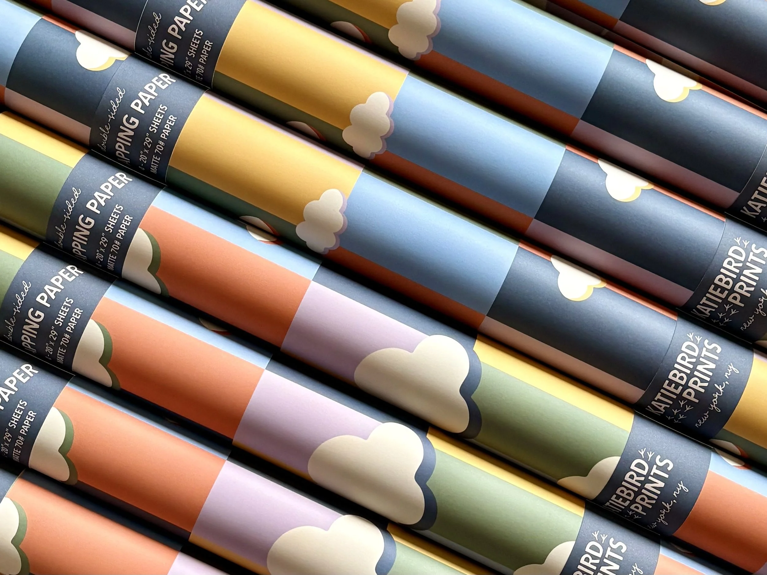 Rolls of patterned wrapping paper with cloud and sky designs, stacked diagonally.