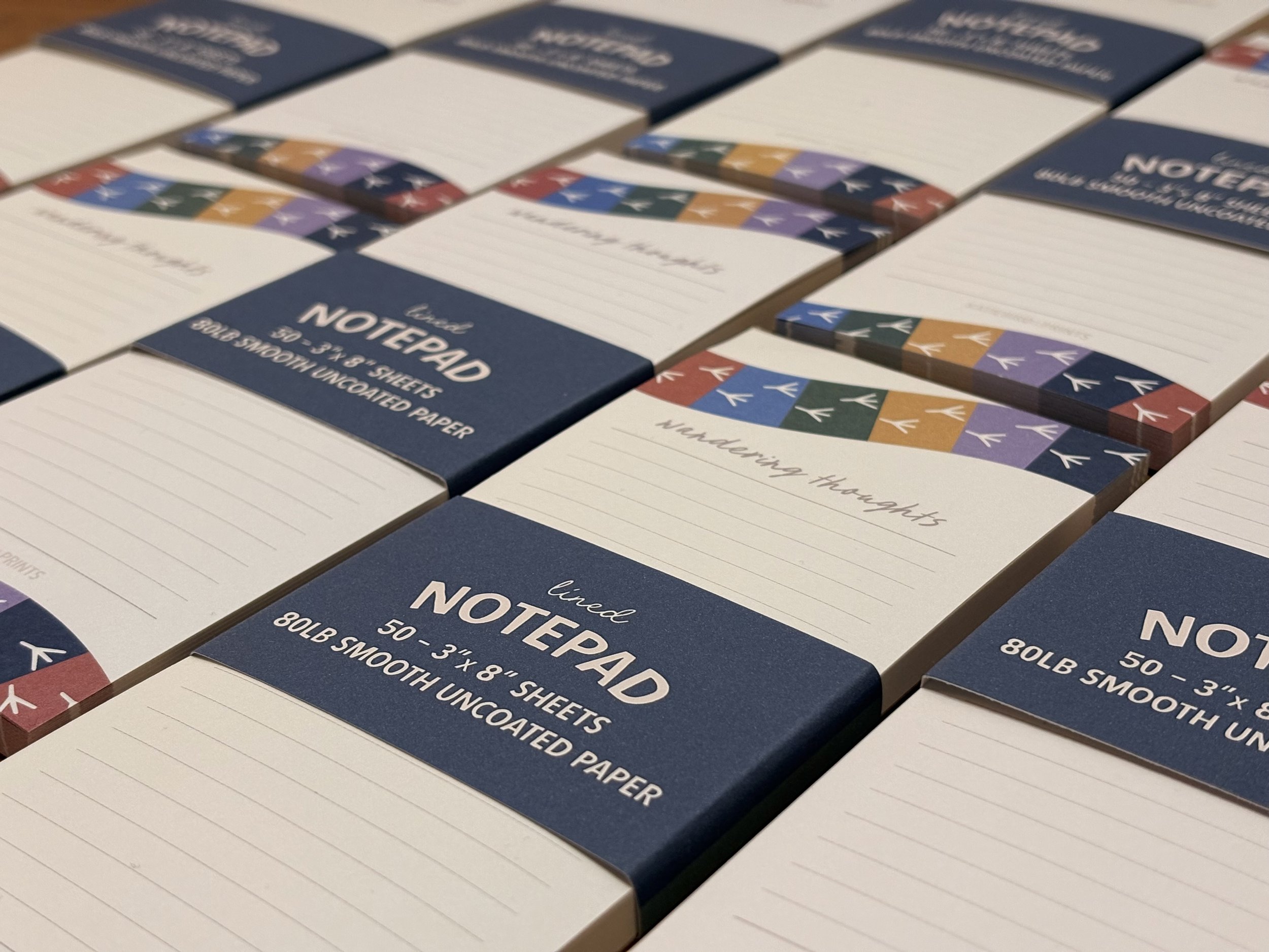 Multiple boxes of lined notepads with colorful geometric designs on the top border, arranged in rows.