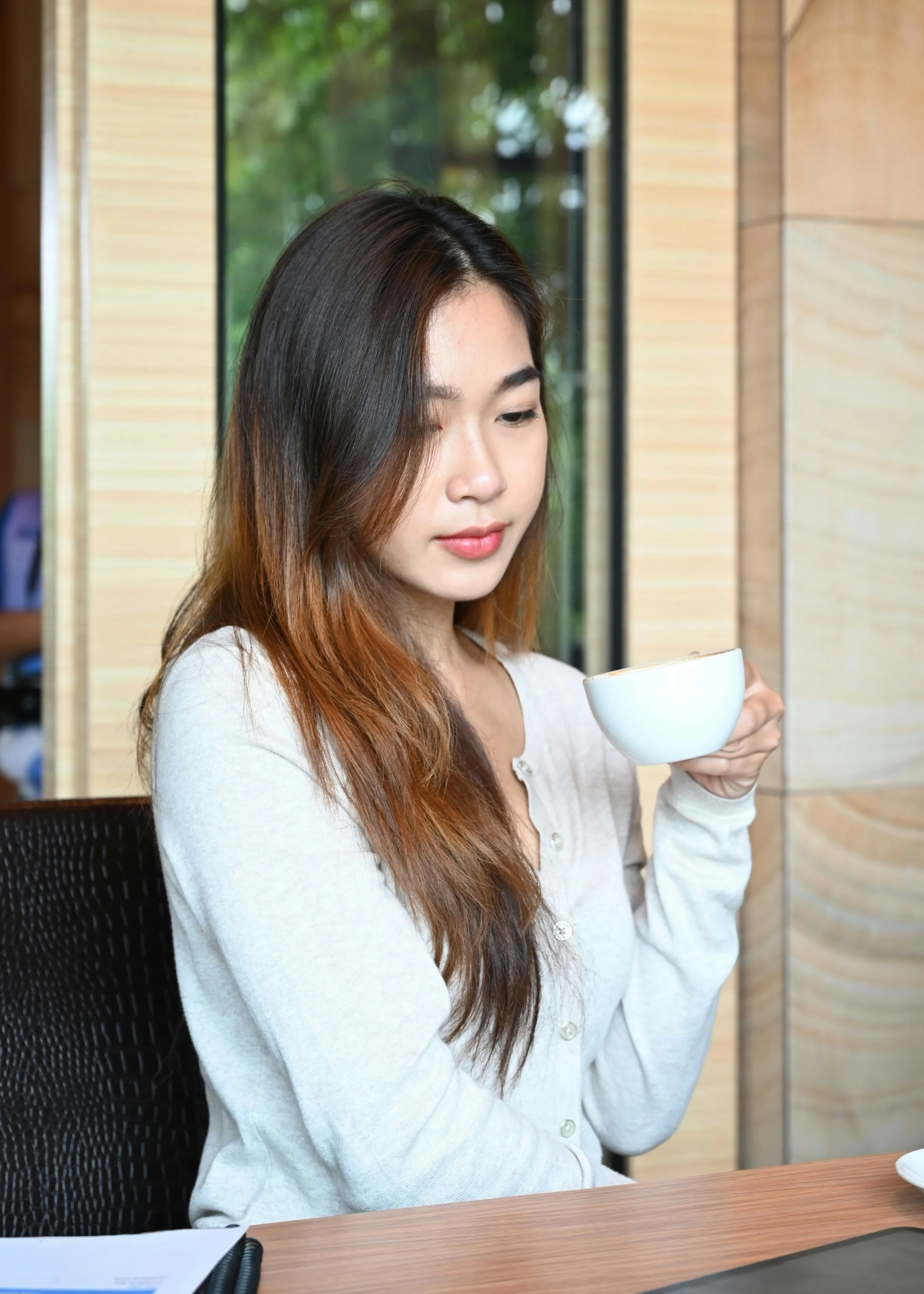 Young woman in office environment looking reflective while drinking tea