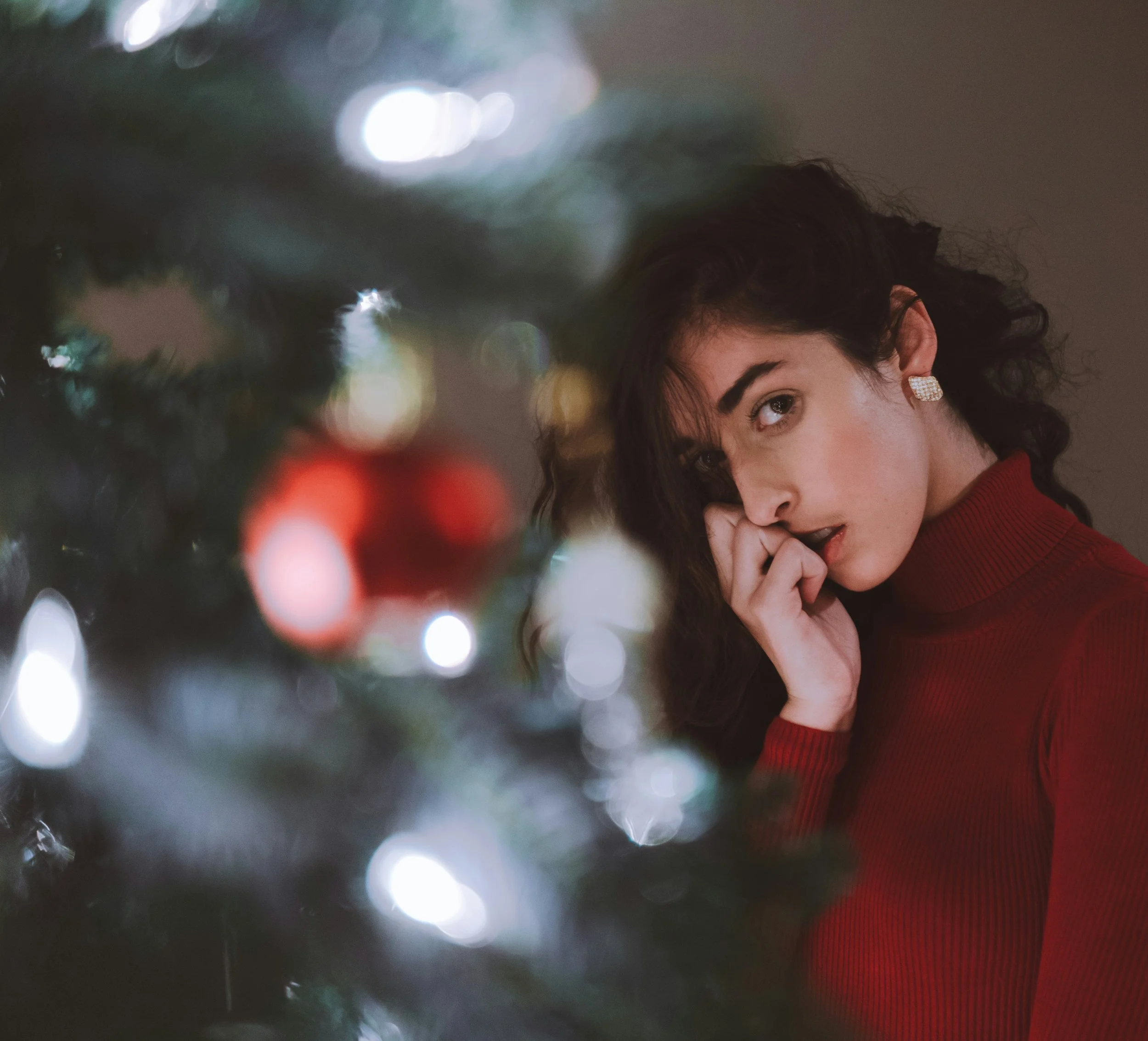 Woman with knuckles against her face with blurred christmas tree behind her Internalizer coping strategy learned as children and how they shape family dynamics during the holidays